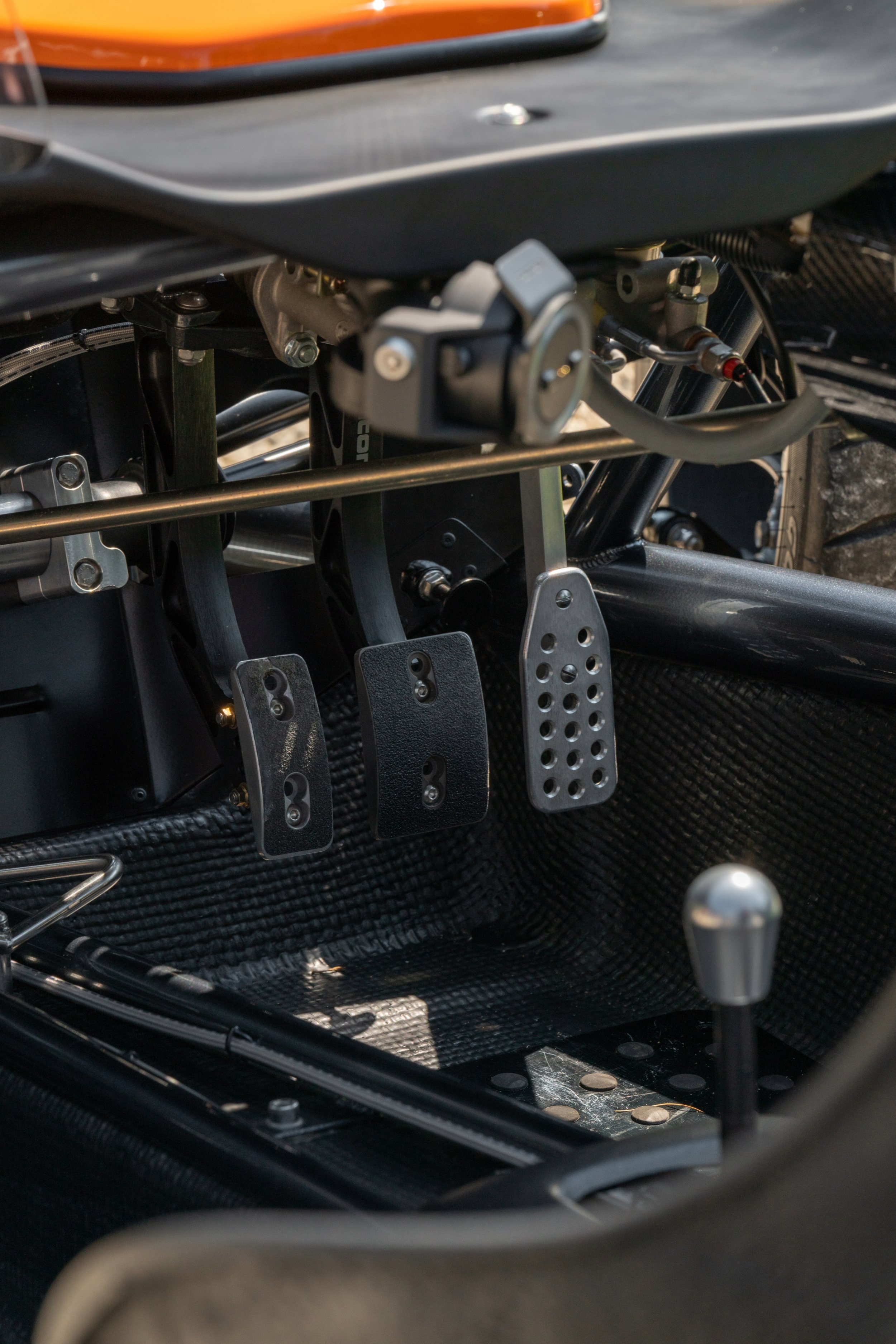 Close-up of the foot pedals and interior of a race car, showing three pedals, a gear shifter, and part of the dashboard.