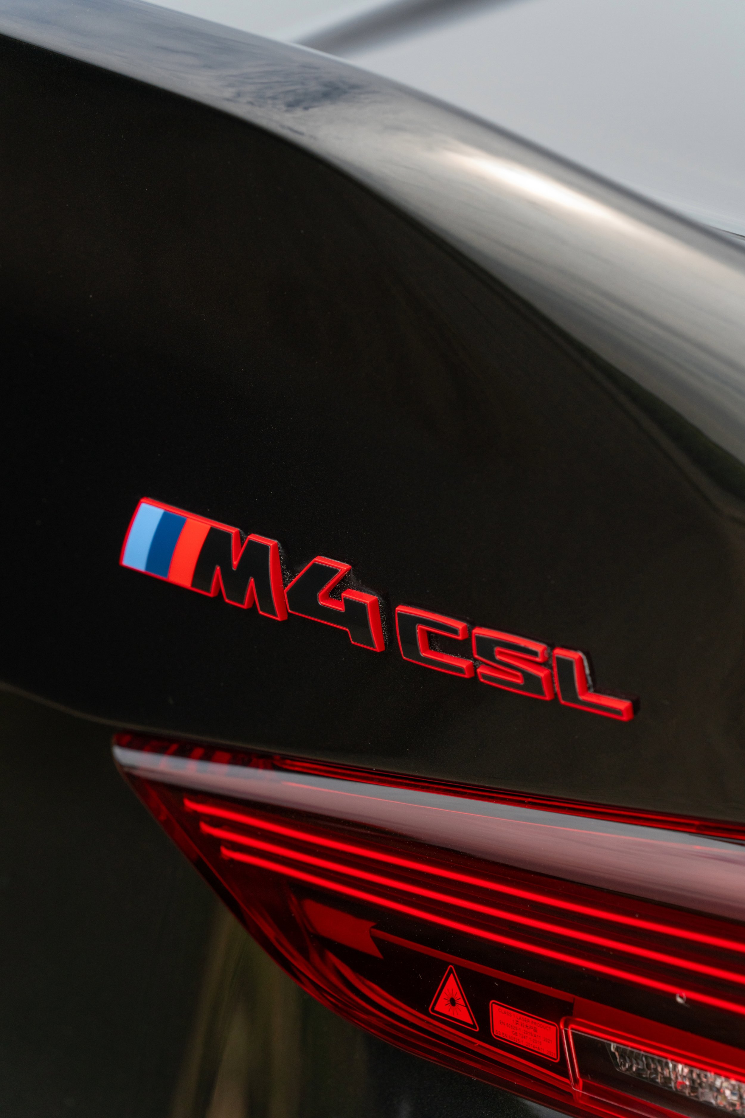 Close-up of a BMW M4 CSL badge on a black car, showing the car's model and brand emblem.