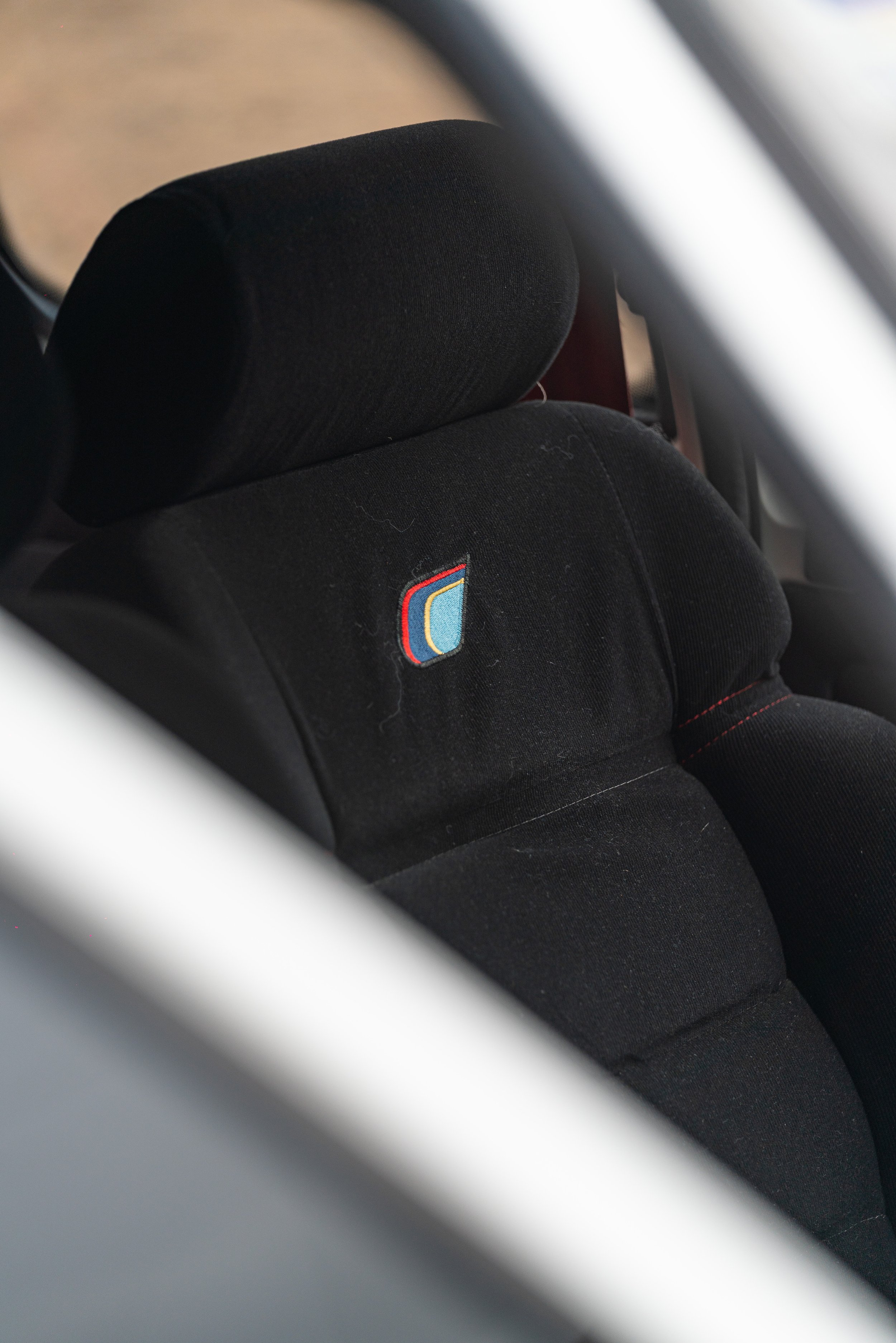 Close-up of a black child car seat with a colorful logo on the fabric in a vehicle interior.