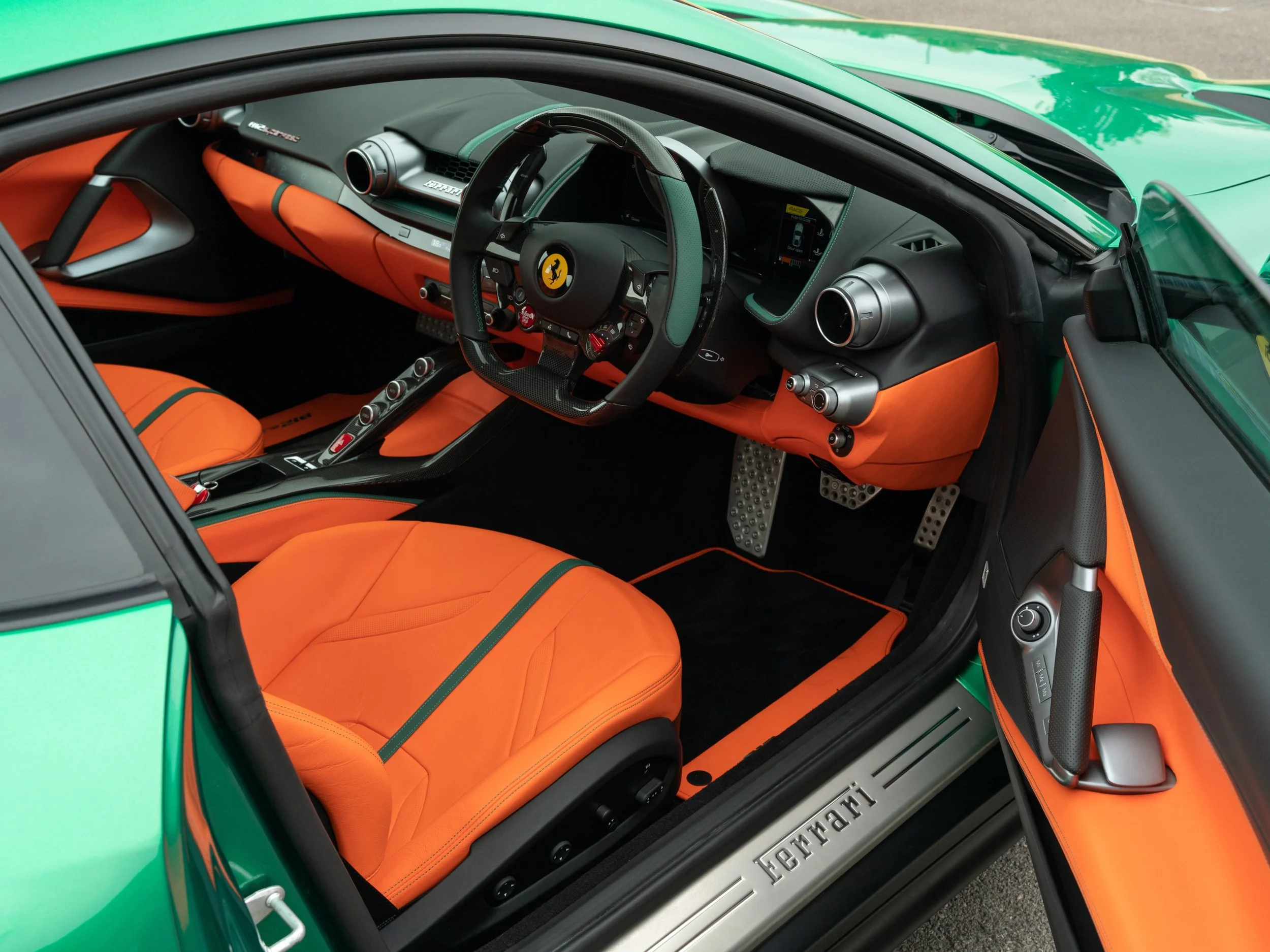 The interior of a luxury sports car with orange leather seats and black dashboard, steering wheel with Ferrari logo, and green exterior.