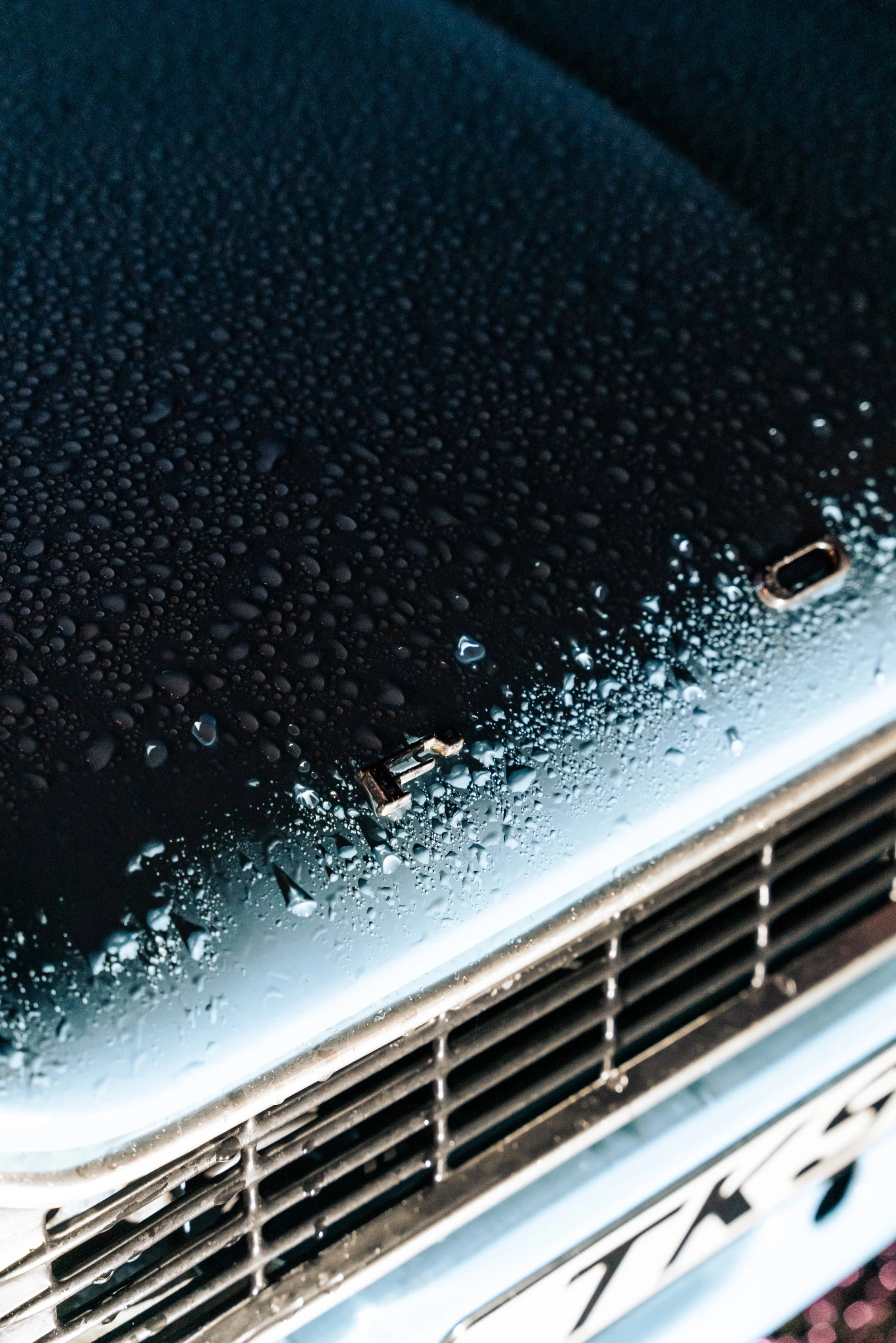 Close-up of a black vehicle with water droplets on its surface and the word 'FAIR' on the front grille.
