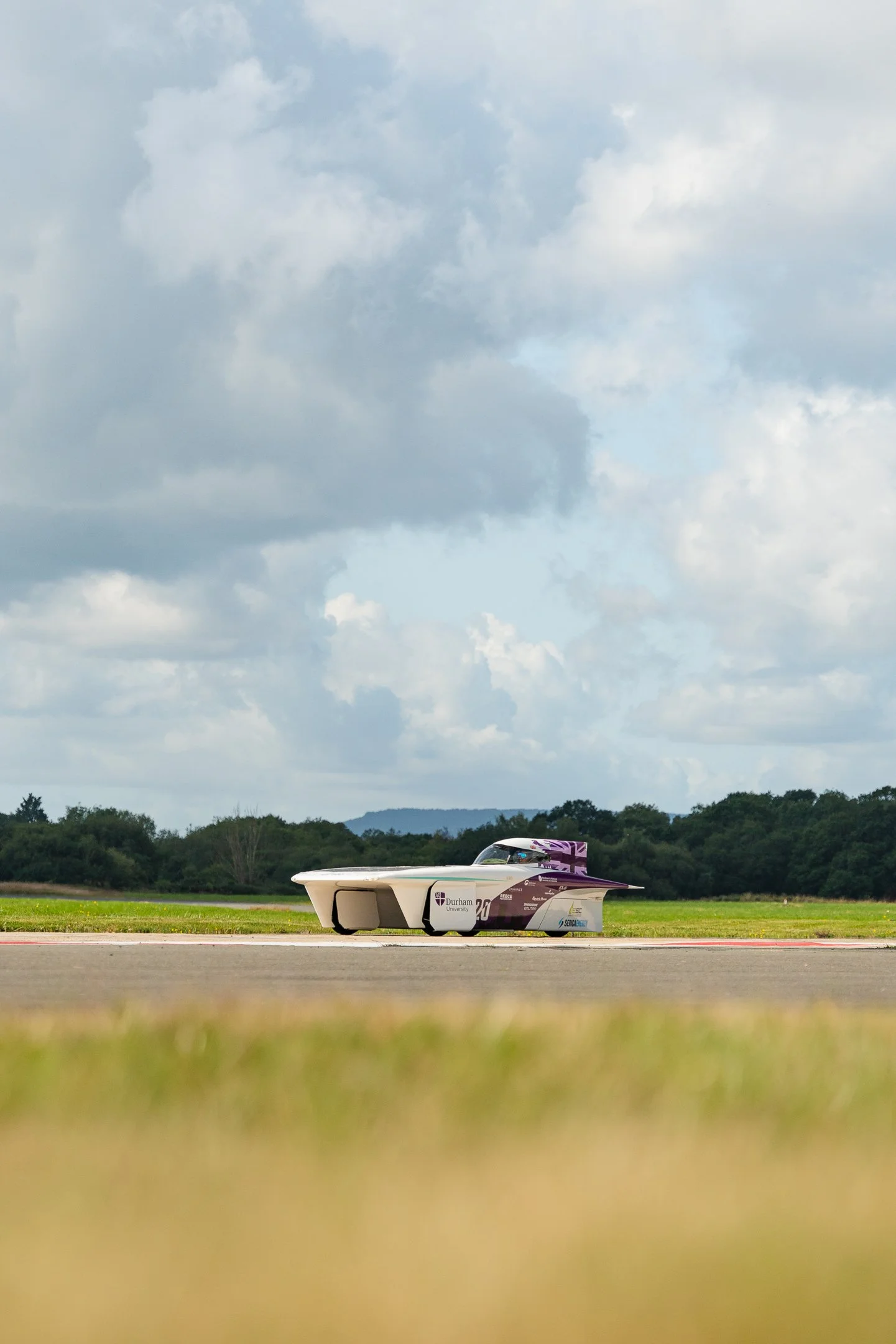 A futuristic vehicle on an airstrip with a cloudy sky and distant green trees.