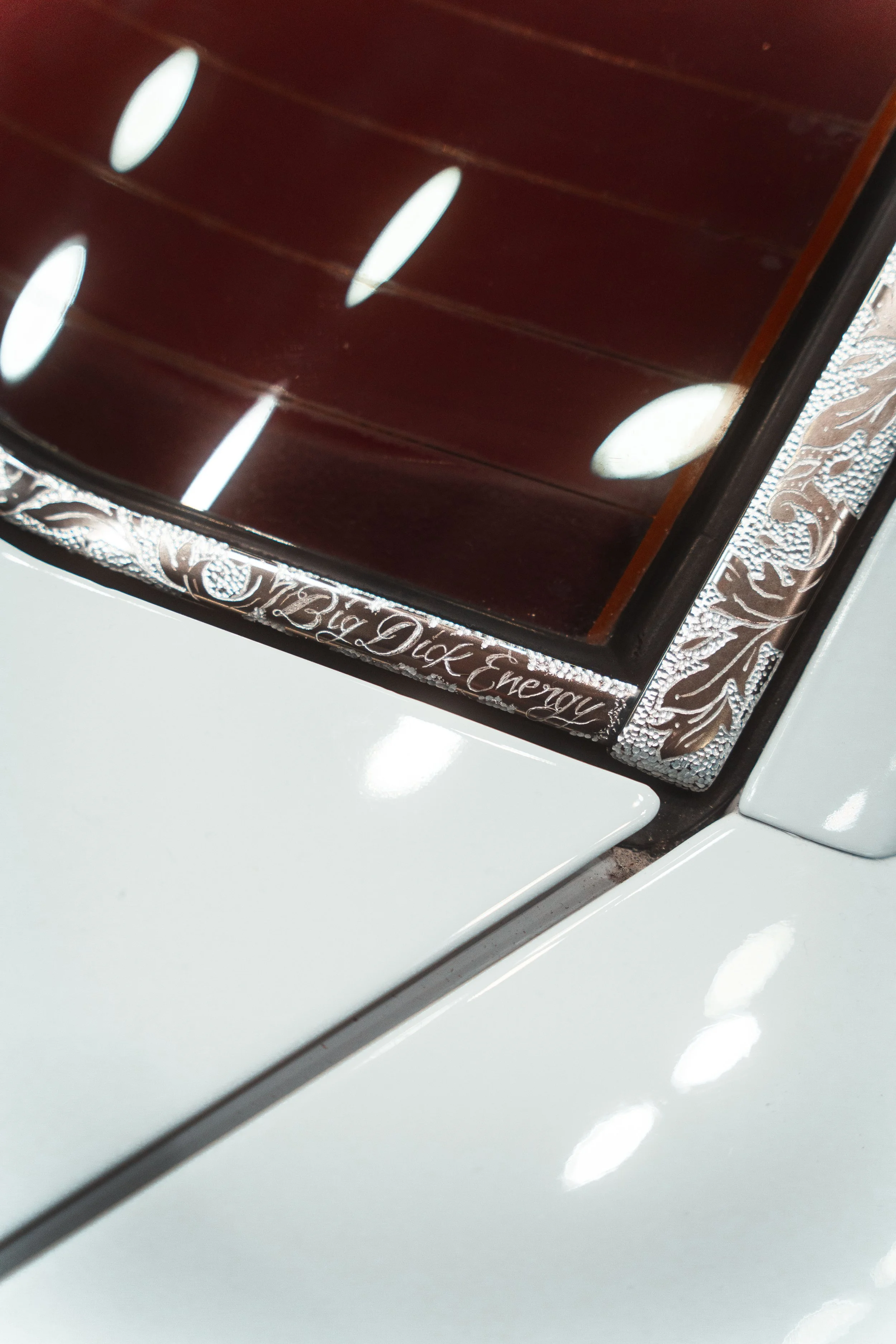 Close-up of a white Tesla car with a decorative trim that reads "Big Dick Energy" near the rear window.