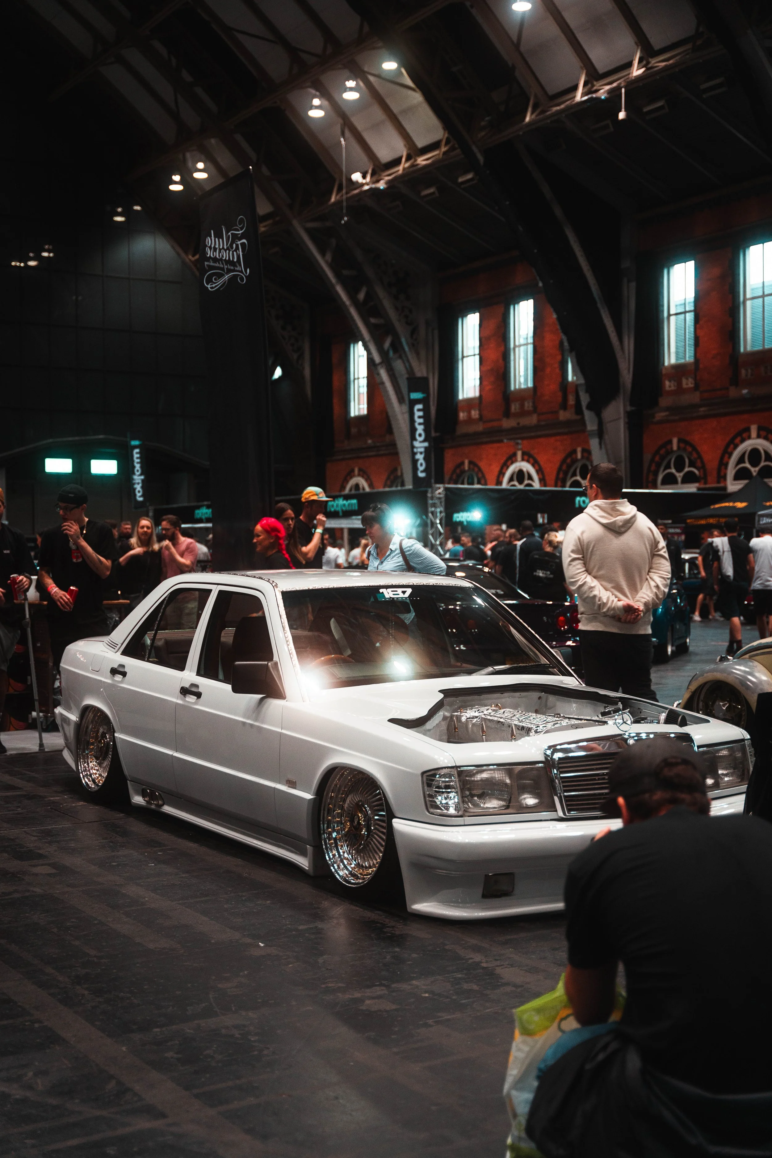 A customized white vintage Mercedes-Benz with lowered suspension and large polished rims on display at an indoor car show.