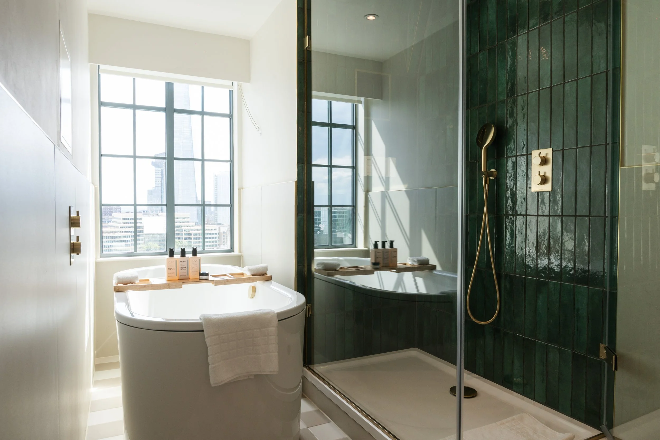 Modern bathroom with a large bathtub near a window and a separate glass-enclosed shower with green tiles.