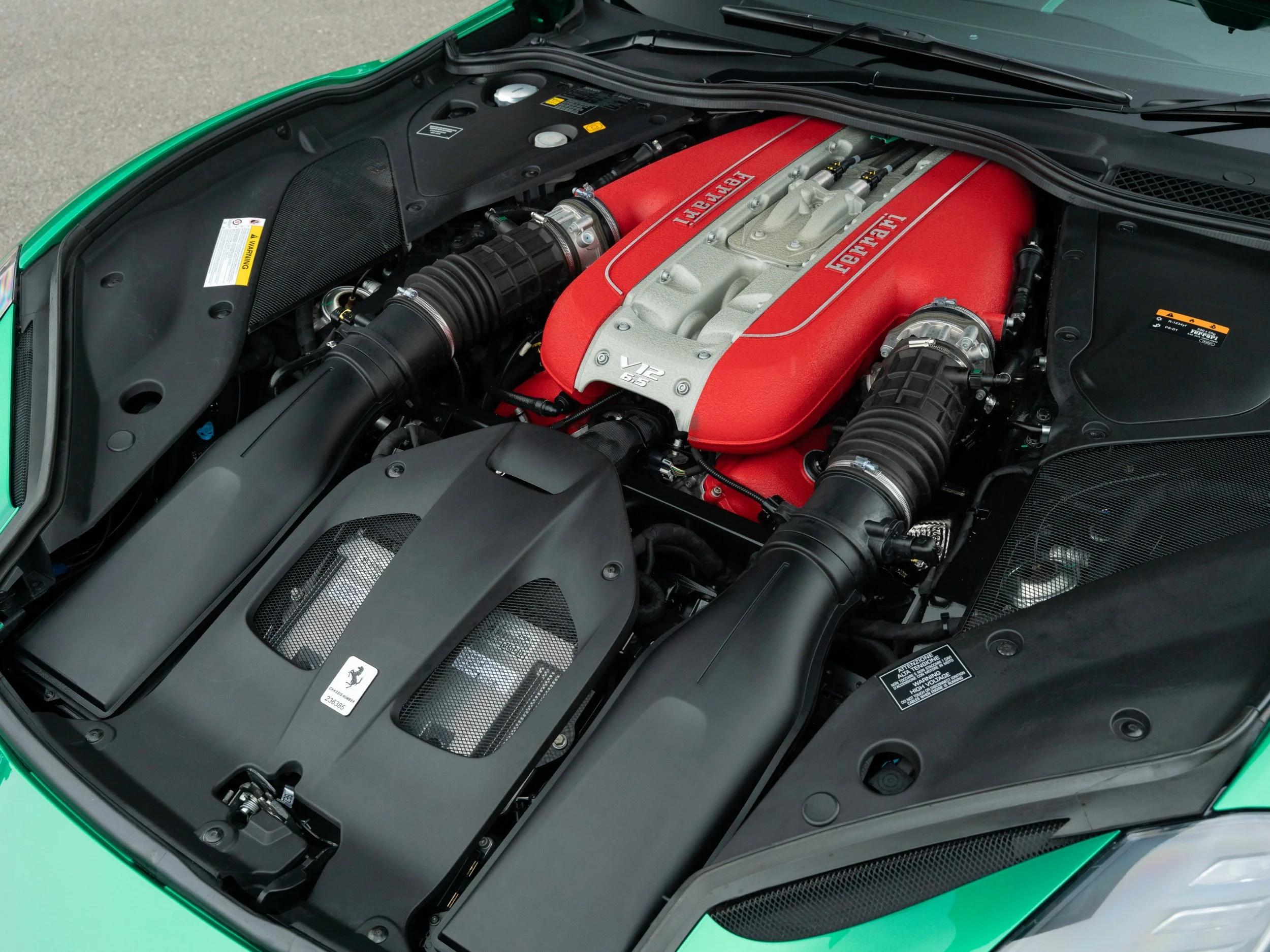 Engine bay of a Ferrari car featuring a red engine cover with Ferrari branding, black intake ducts, and various mechanical components.