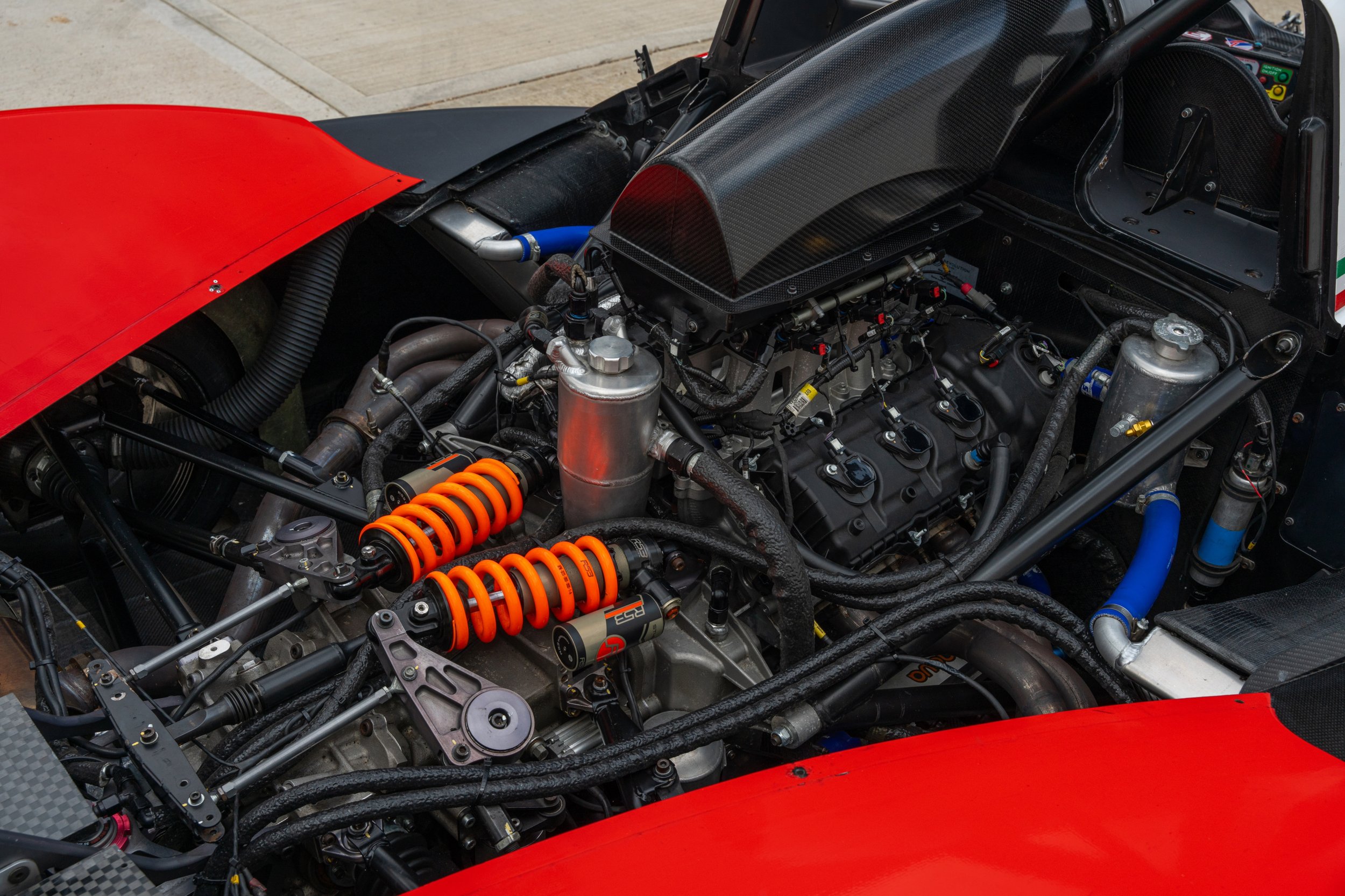Close-up of a race car engine with black, silver, and orange components, surrounded by red body panels.