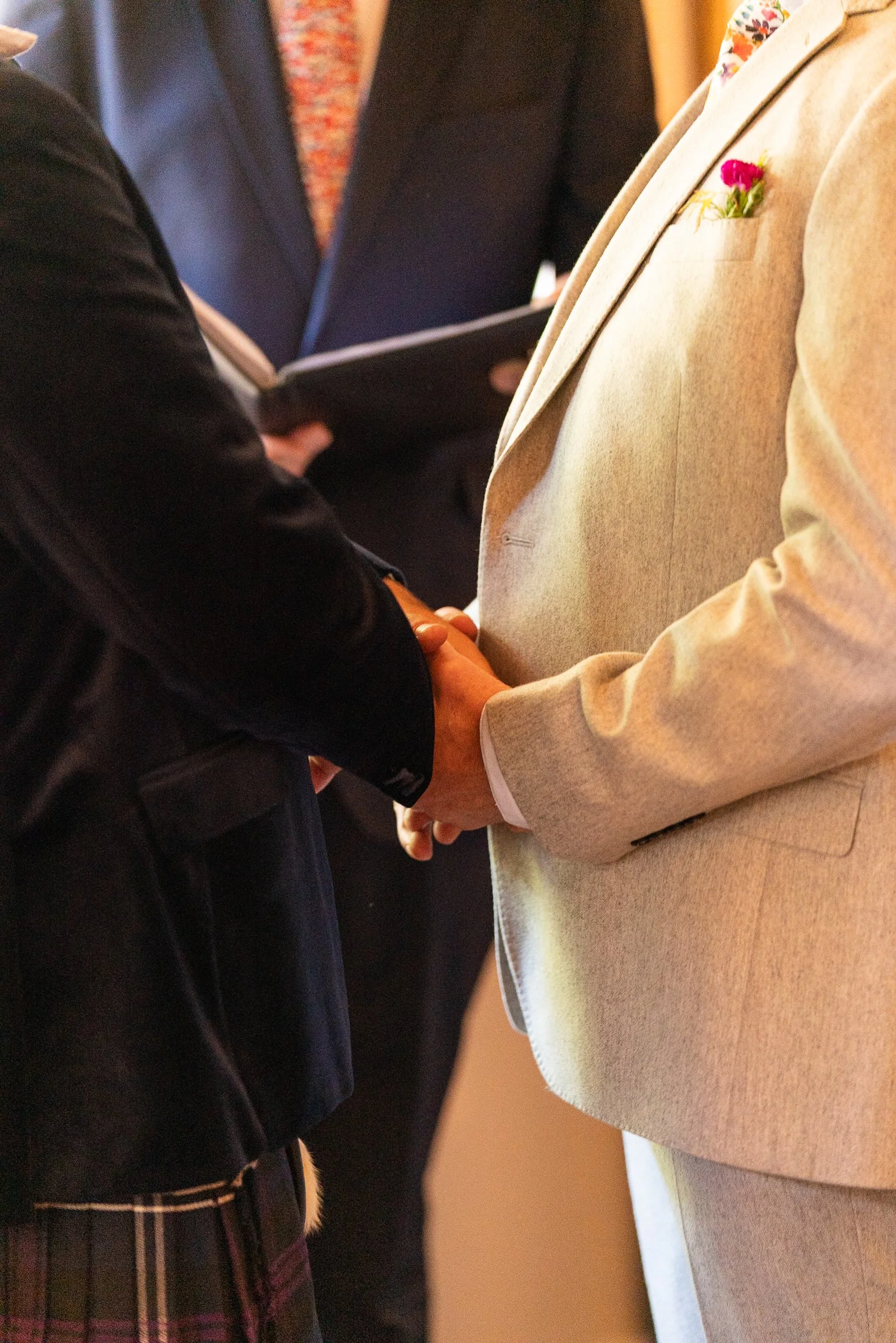 Two individuals holding hands during a ceremony with an officiant in the background.