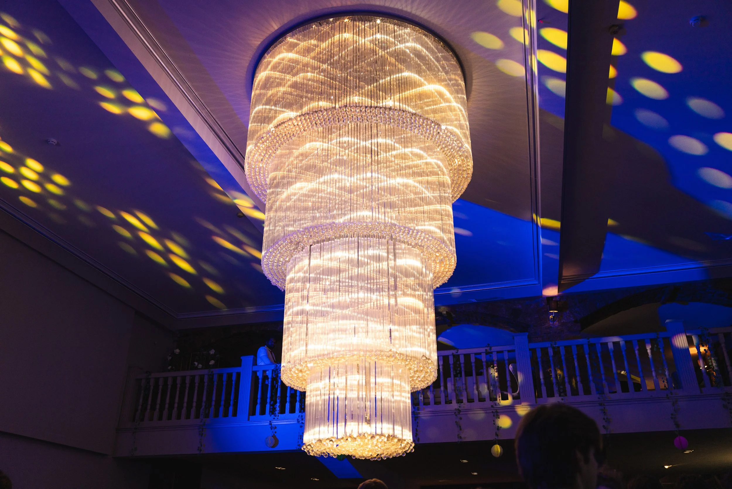 Large, elegant chandelier with cascading tiers of lights and crystals hanging from a ceiling in a dimly lit space.