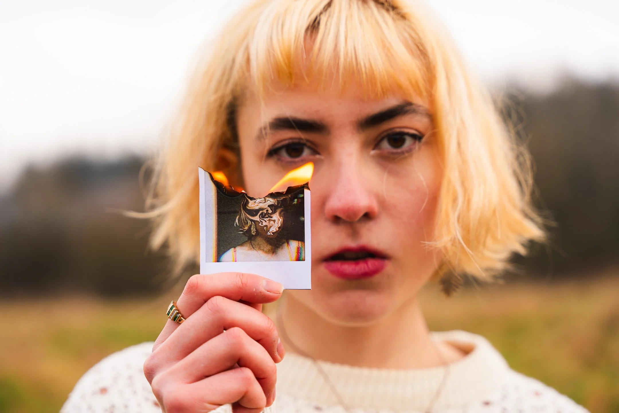 A woman with blonde hair holding a burned photograph outdoors.