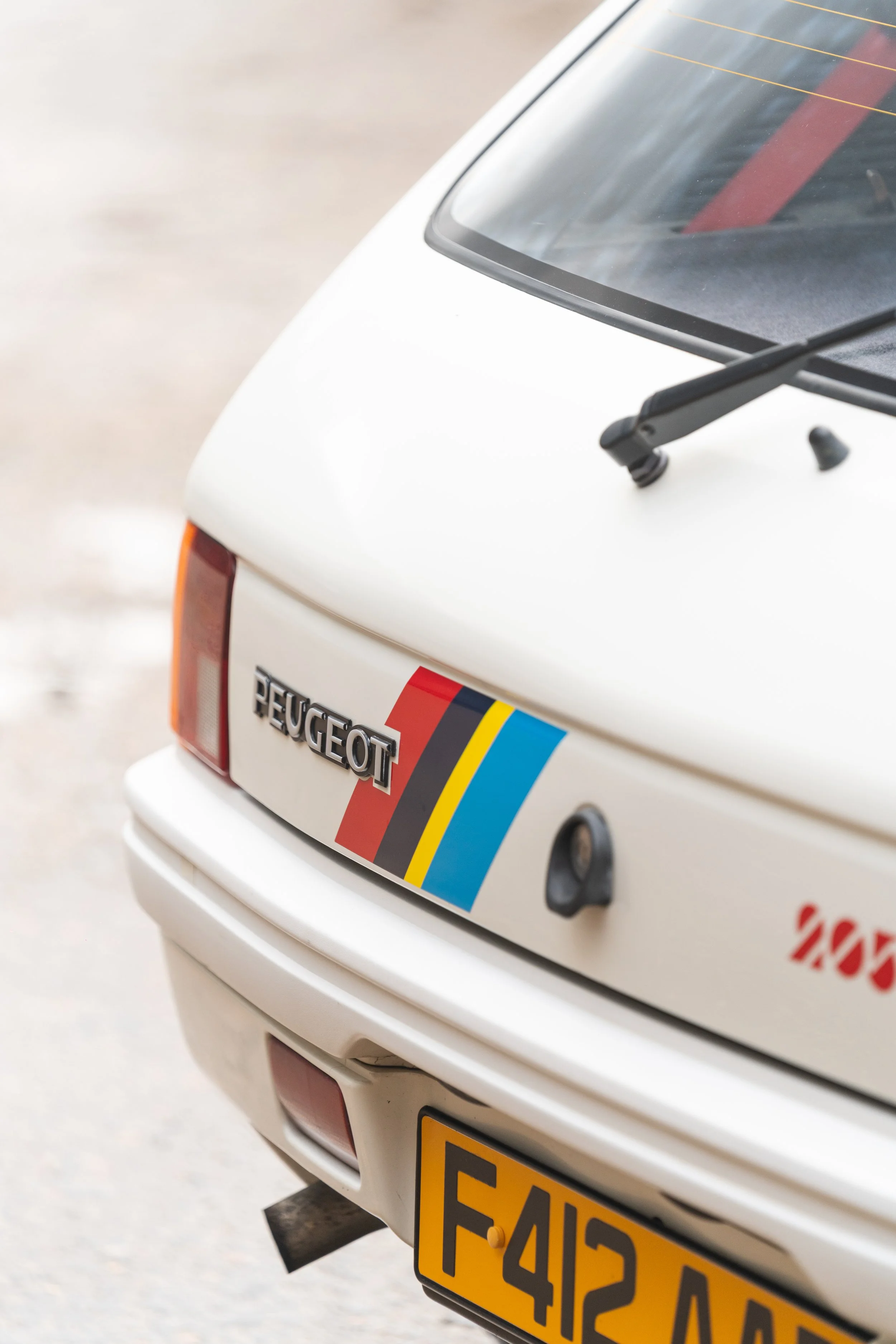 The rear of a white Peugeot car with a colorful sticker and a yellow license plate.