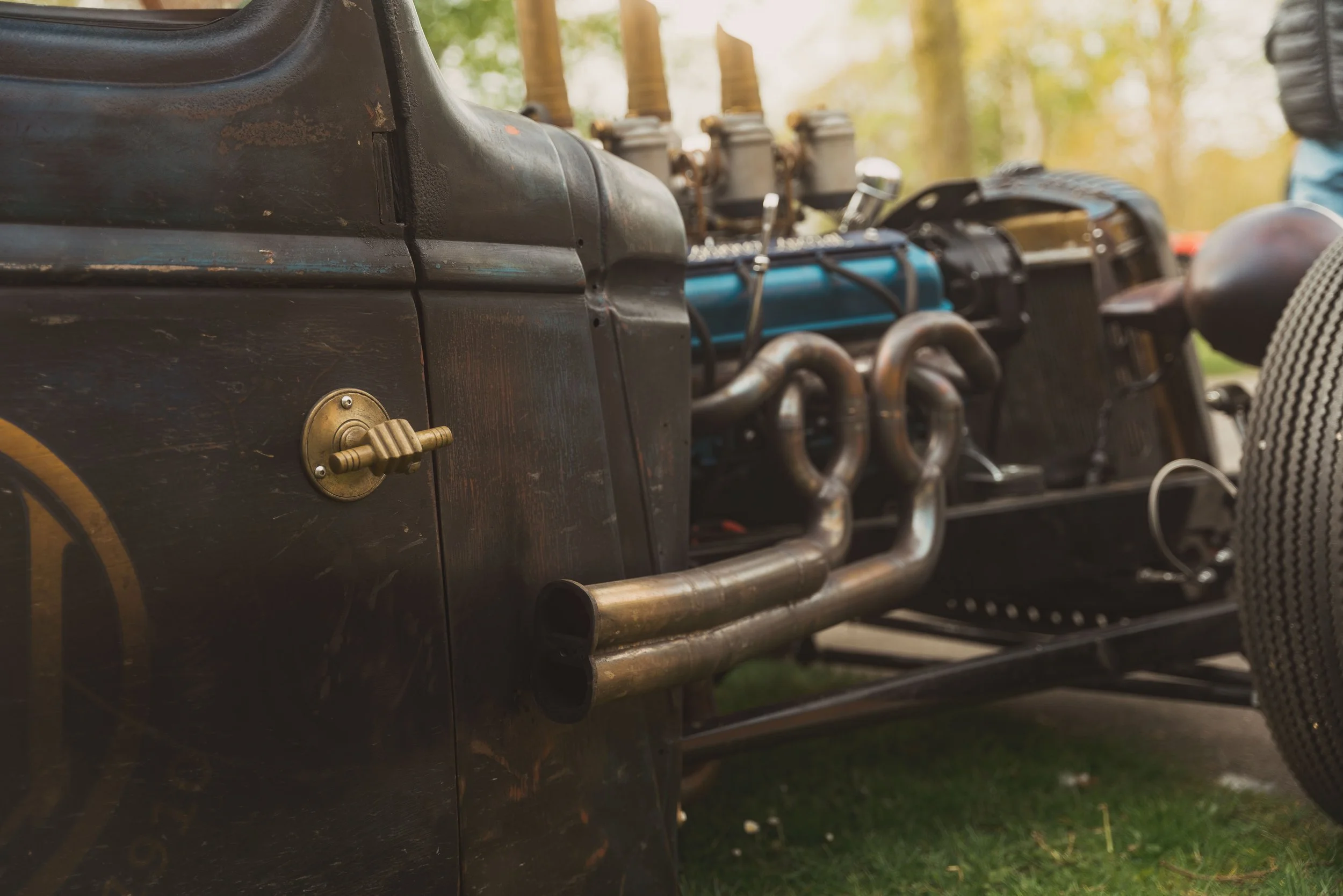Close-up of a vintage race car engine showing metal pipes and components, with a black body and a textured seat in the foreground.