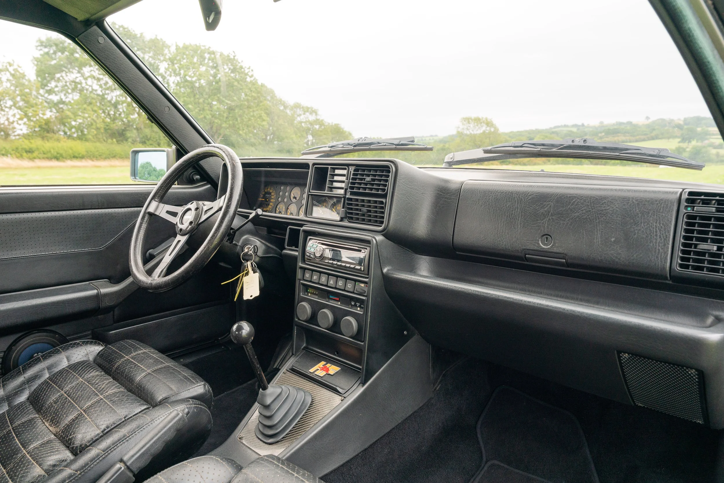 Interior of a vintage vehicle, showcasing a black dashboard, a steering wheel, a gear shift, and a plaid seat.