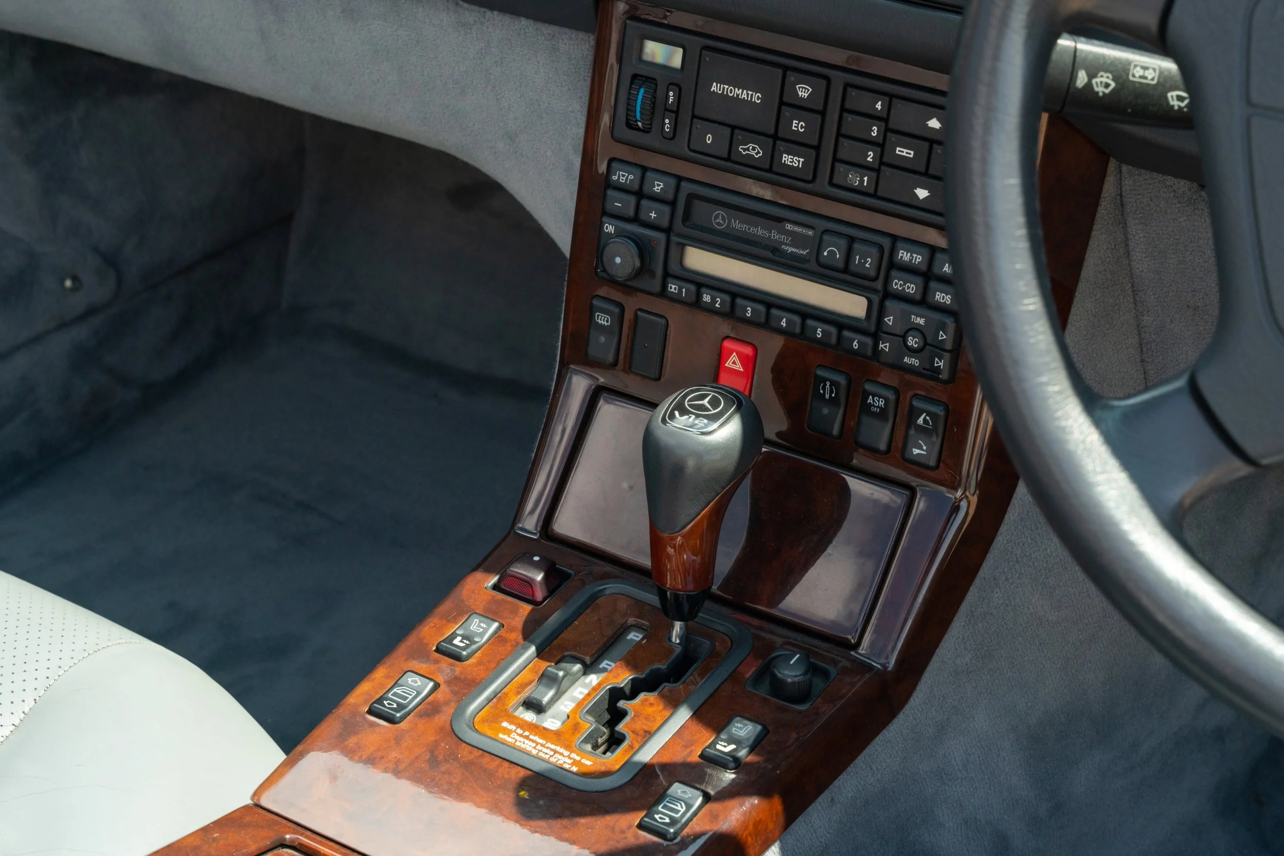 Interior view of a luxury Mercedes-Benz car dashboard and gear shift, featuring wood paneling, various control buttons, and a steering wheel.