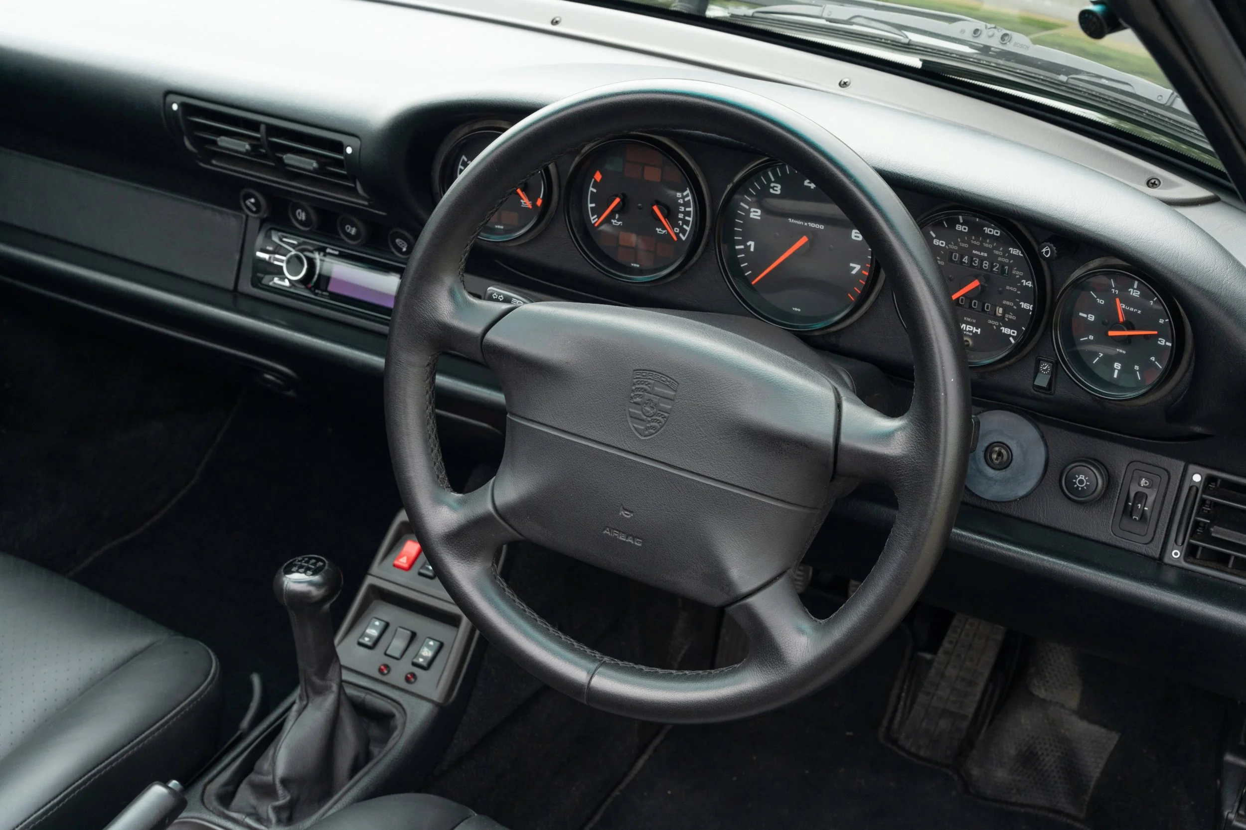 The interior of a classic Porsche car featuring a black dashboard, steering wheel with Porsche emblem, and analog gauges including speedometer, tachometer, and fuel gauge.