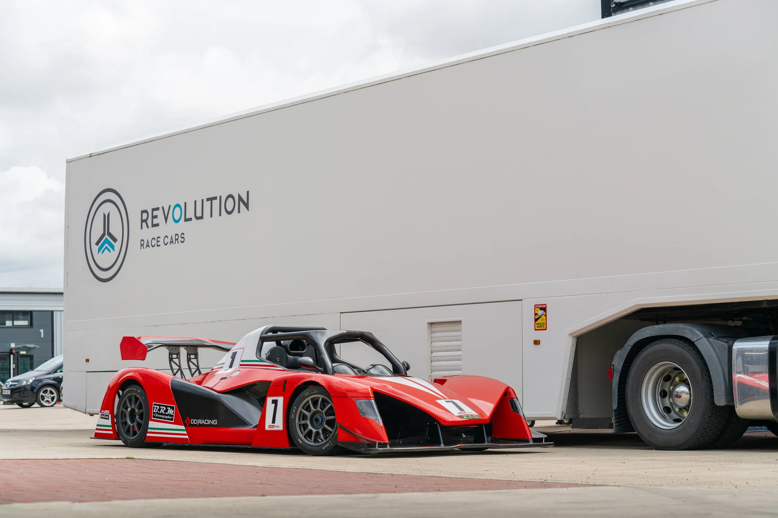 Red race car with the number 7 parked beside a white truck with 