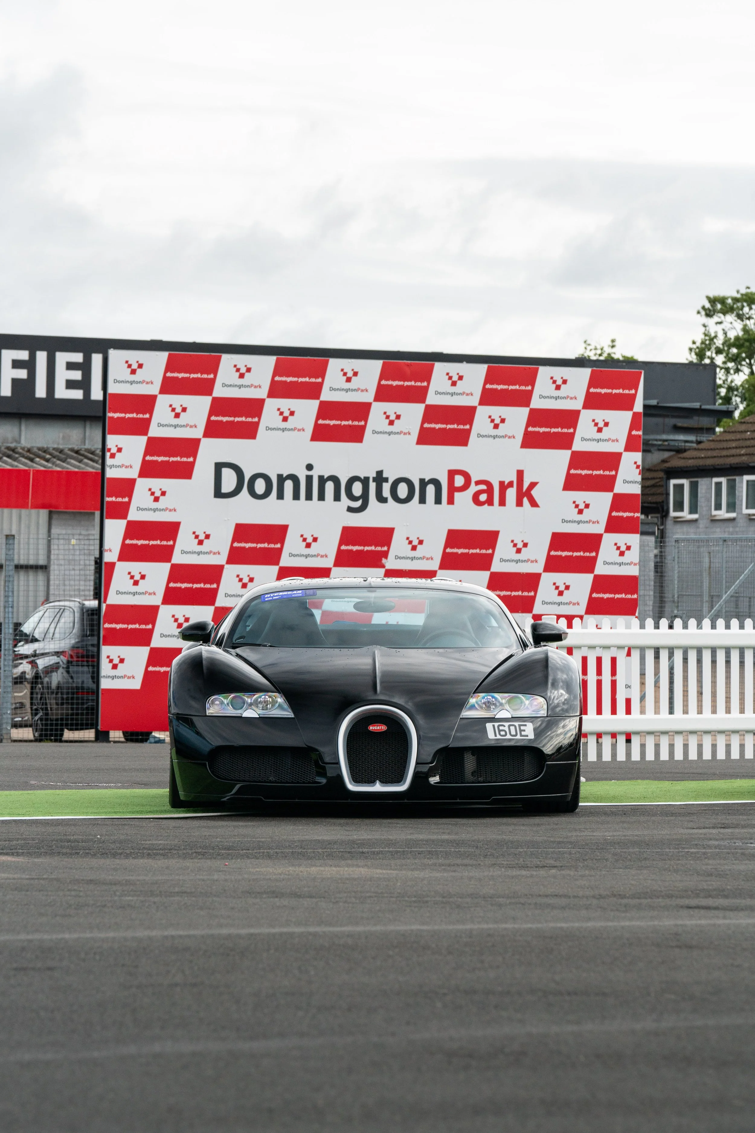 A black Bugatti sports car parked on a racetrack at Donington Park, with a large sign displaying Donington Park in the background.