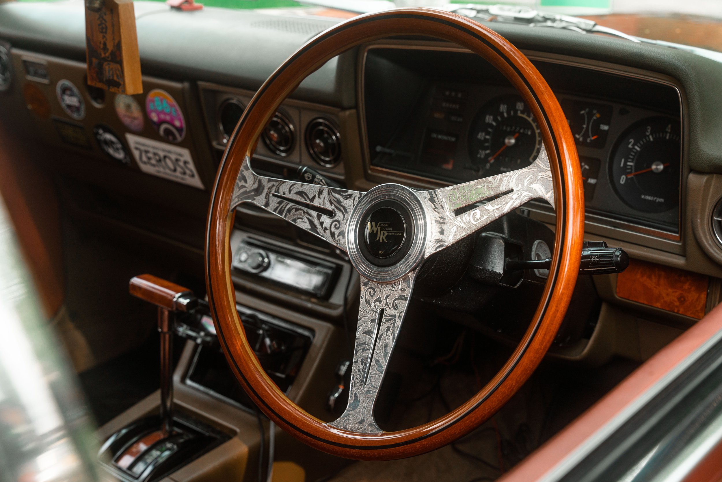 Inside a vintage car with a wooden steering wheel, dashboard, and various gauges and stickers.