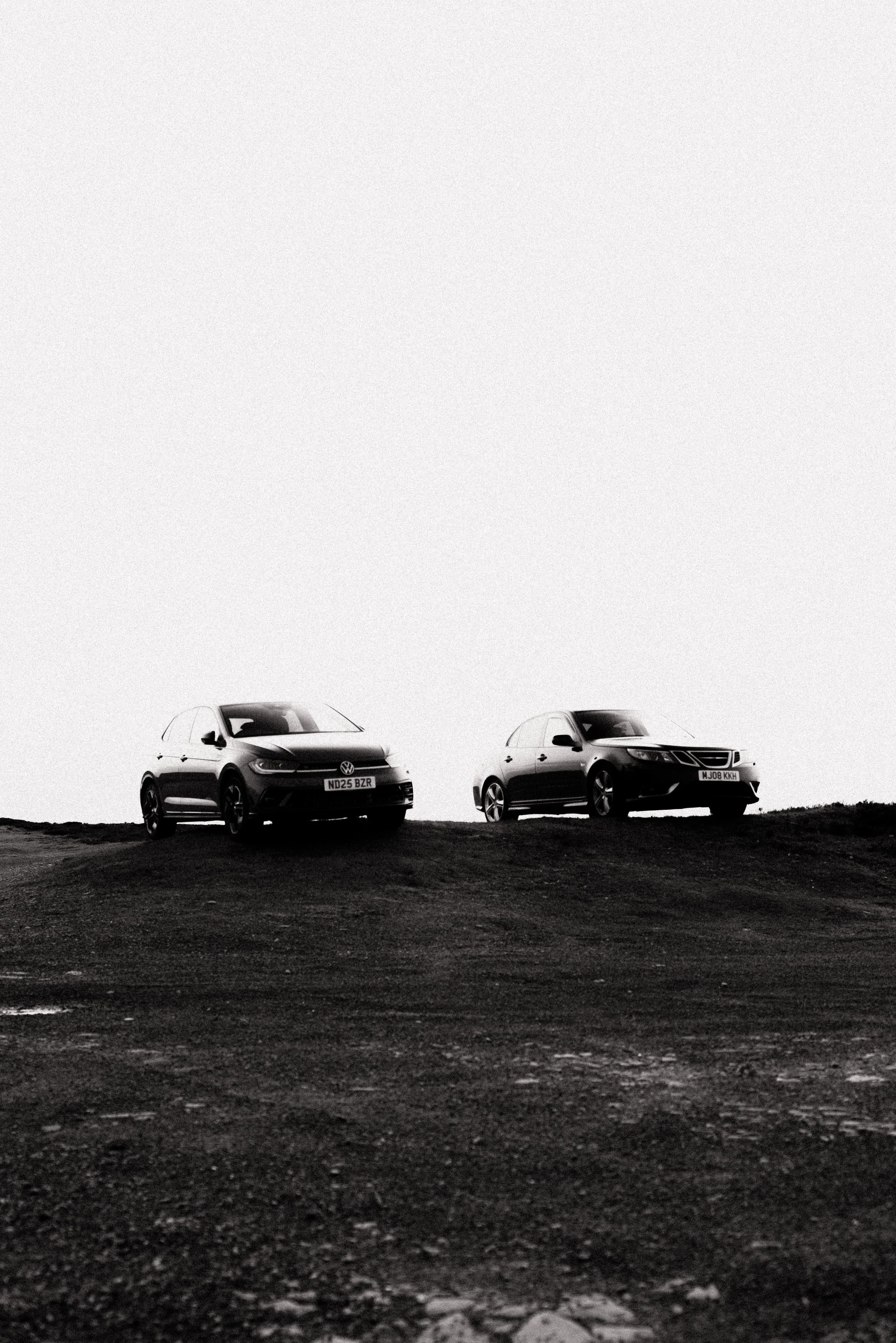 Two cars parked on a dirt surface under a bright sky.