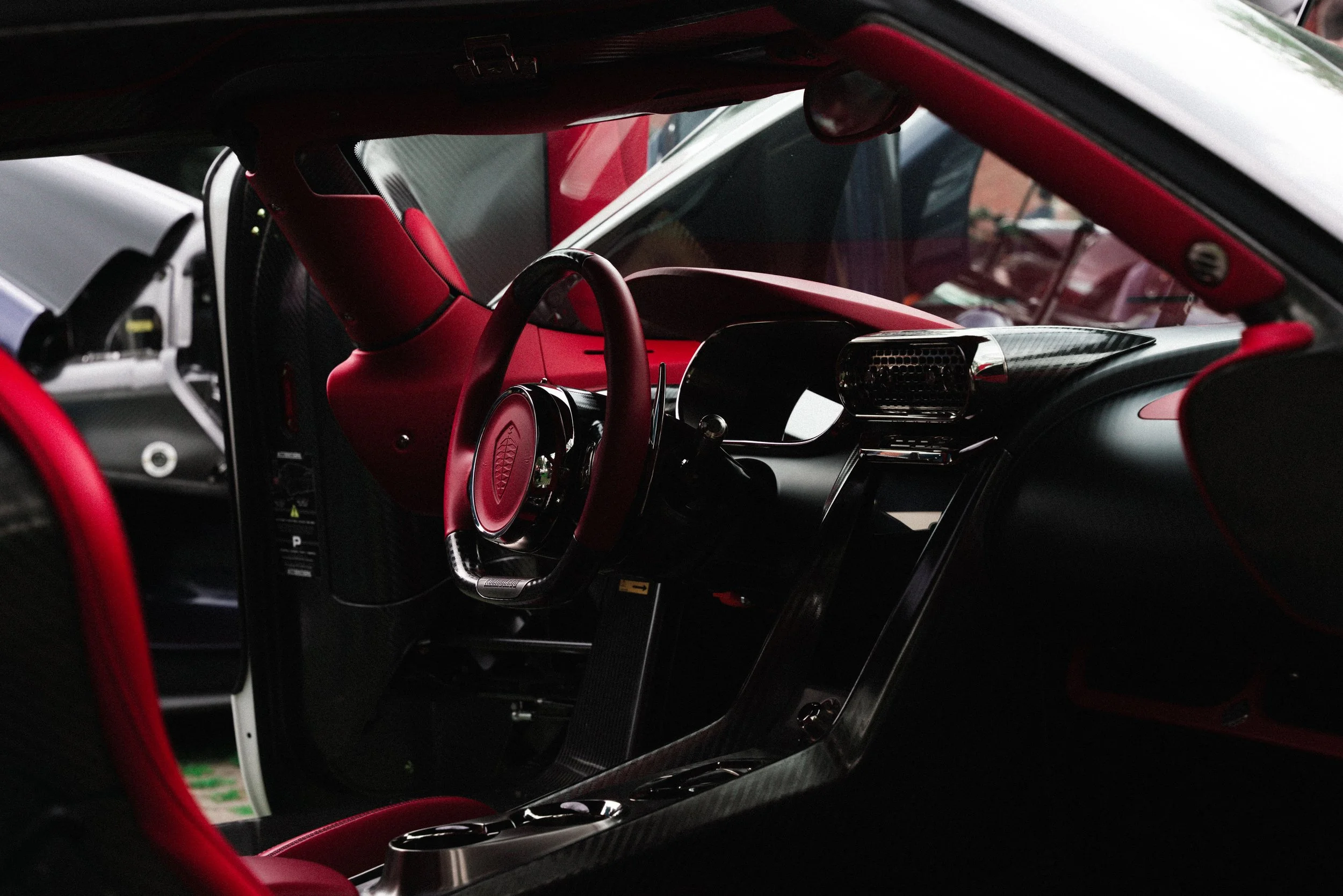 Interior view of a racing car with red and black leather upholstery, carbon fiber dashboard, and steering wheel.