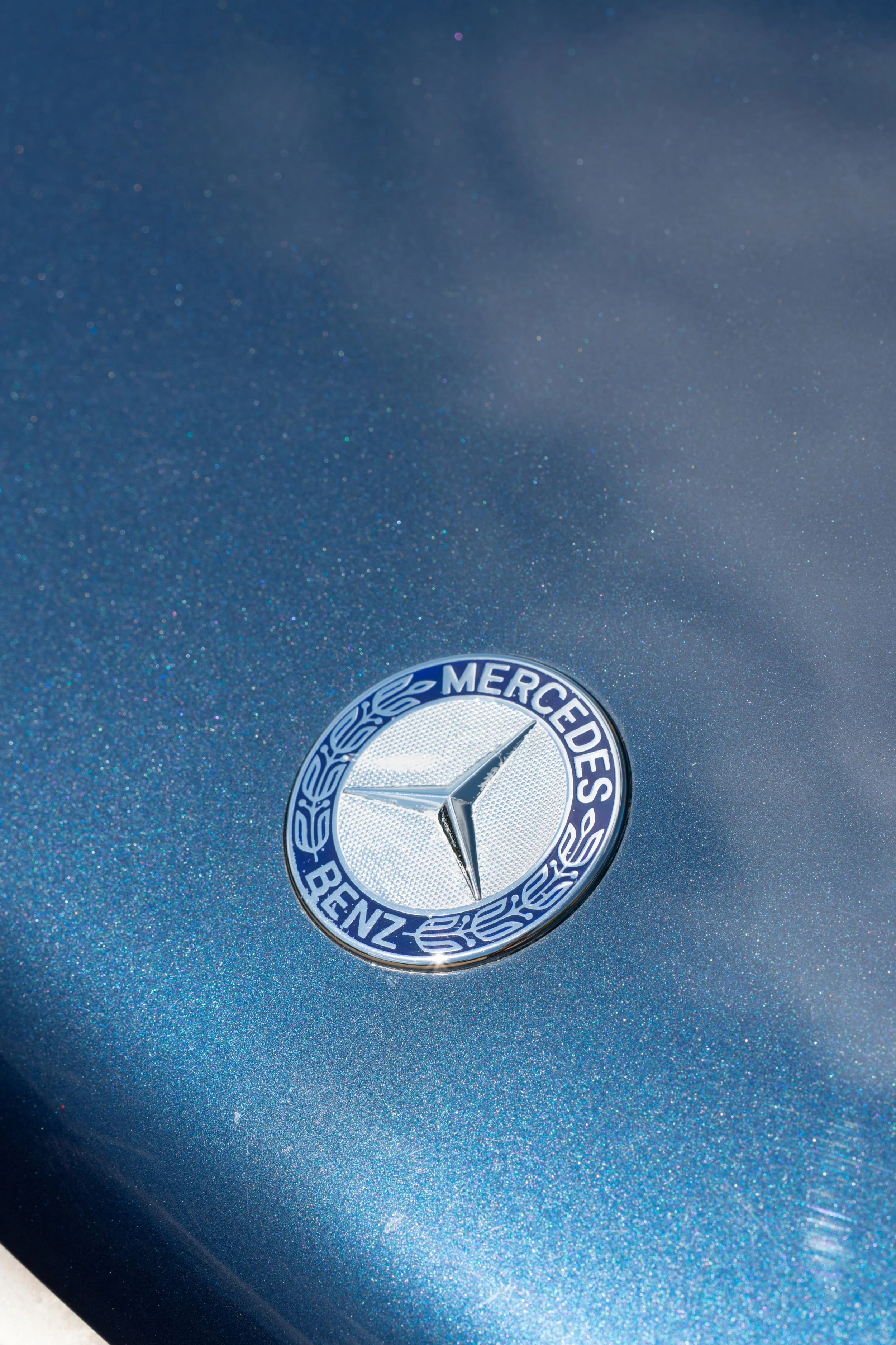 Close-up of a Mercedes-Benz logo on a metallic blue car surface.