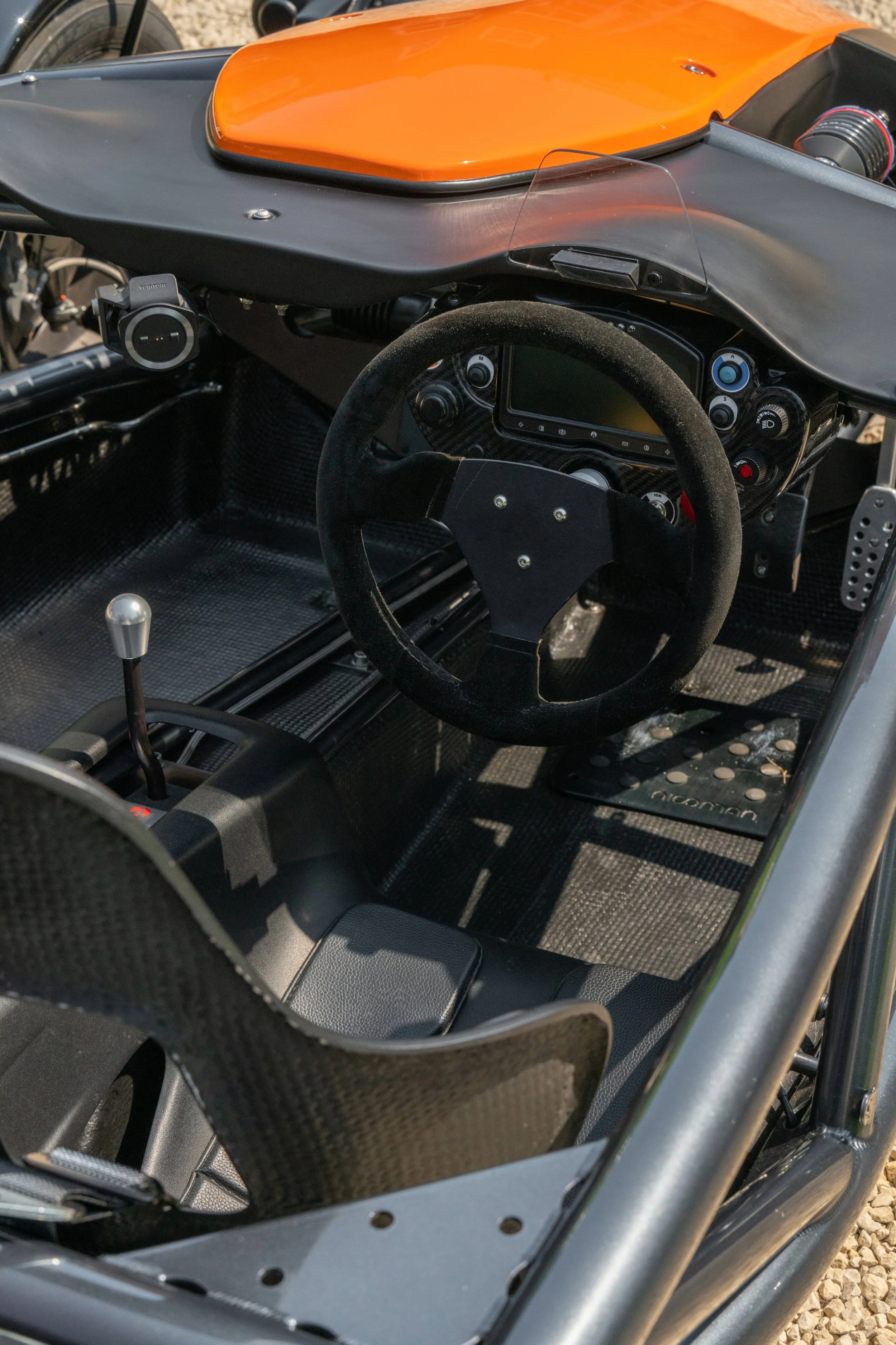 Interior view of a race car with a black steering wheel, digital display, gear shifter, and minimalistic cockpit.