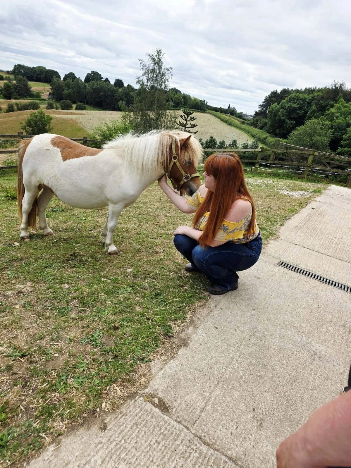 A photograph of a woman and a small miniature pony, she is crouching down and the pony is standing enjoying the attention