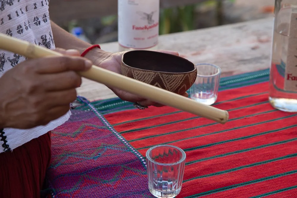 A baked dish with melted cheese and a piece of roasted meat in a brown ceramic bowl on a wooden table outdoors with trees and a mountain in the background.
