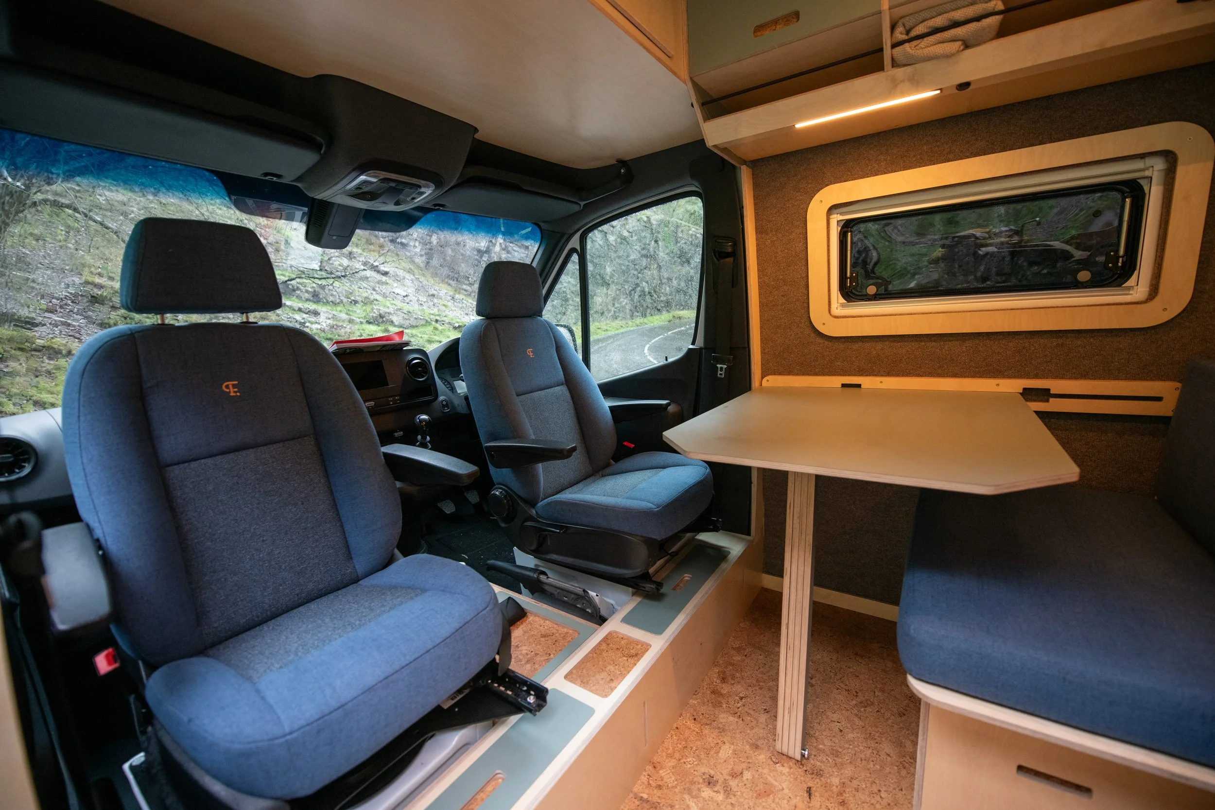 Fern campervan front lounge with swivel seats and dining table, lit by overhead LED strip that provides focused lighting where it is needed most.