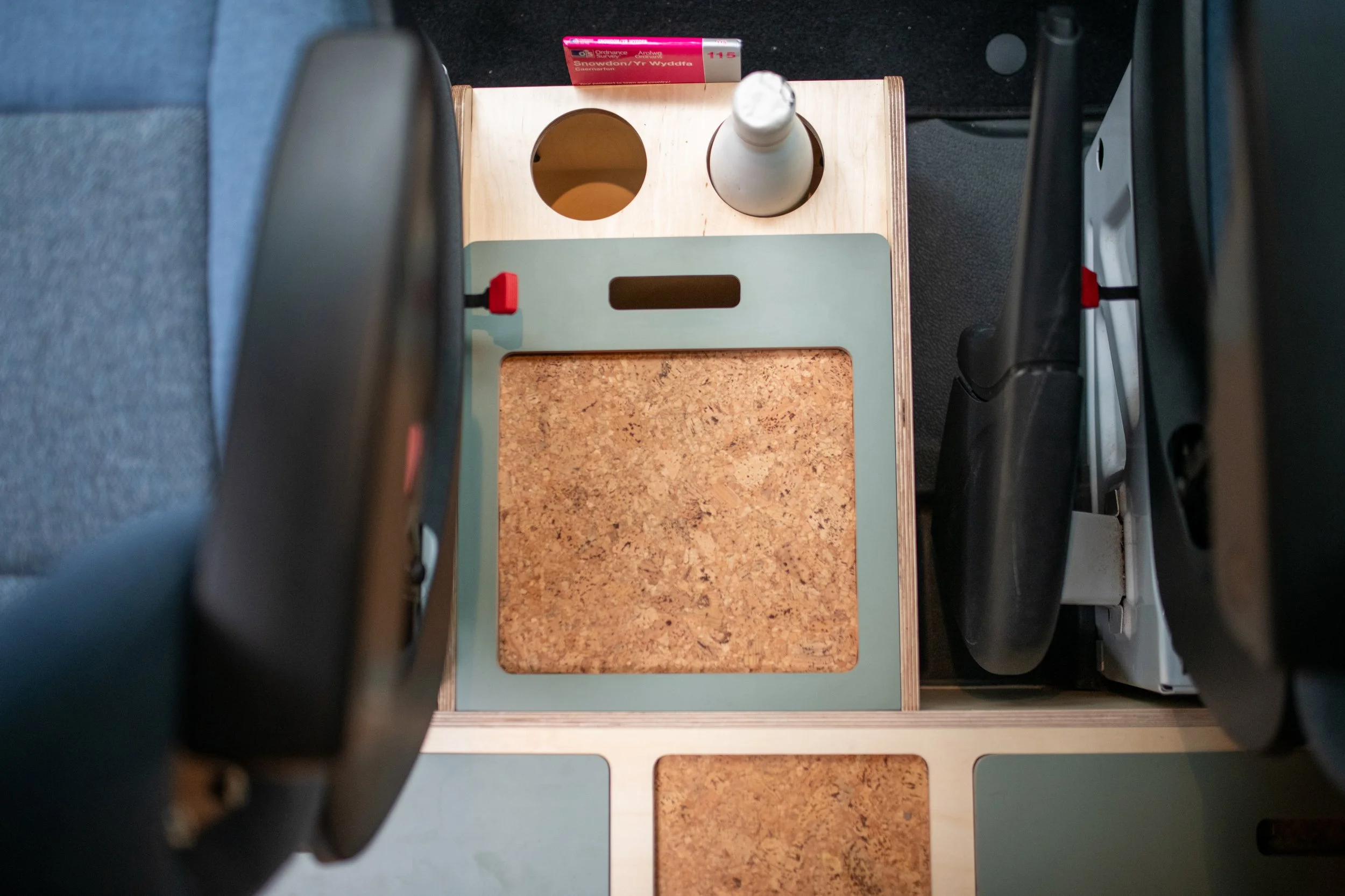 Central storage box with cork lid and twin cup holders between the front seats of a Fern campervan, keeping everyday items tidy and close to hand.