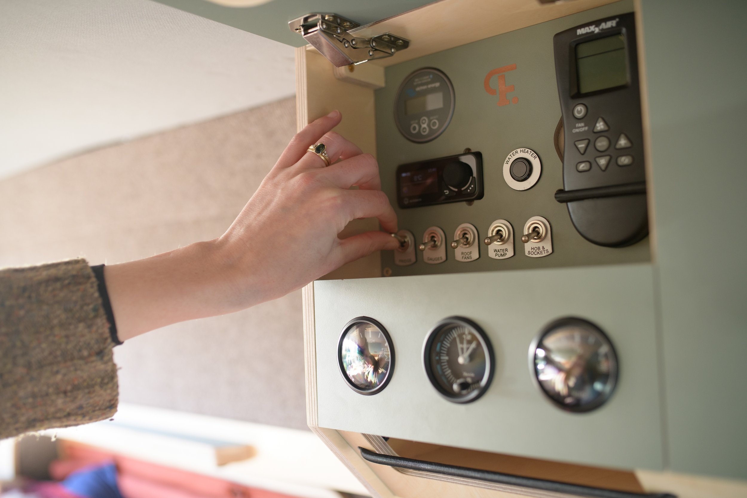 a hand operating the campervan’s overhead control panel, with switches and gauges for easily monitoring and managing off-grid systems.