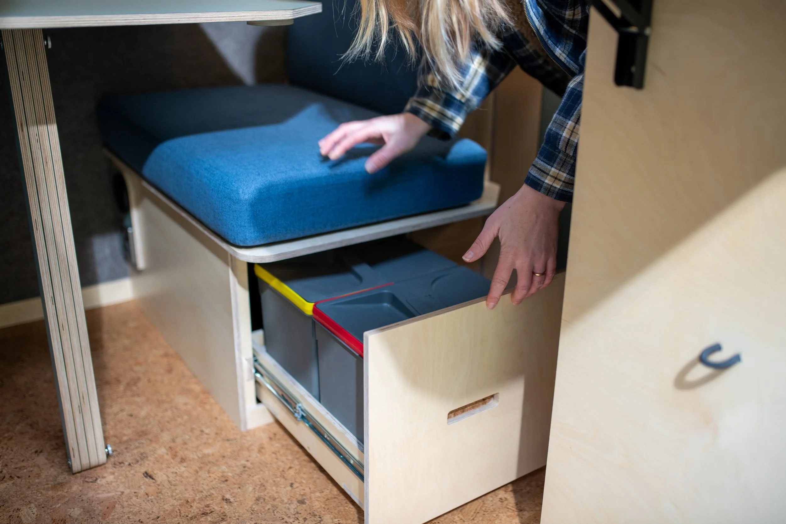 Pull-out drawer under the dining area seat with colour-coded bins, providing integrated waste and recycling storage for self-contained travel.