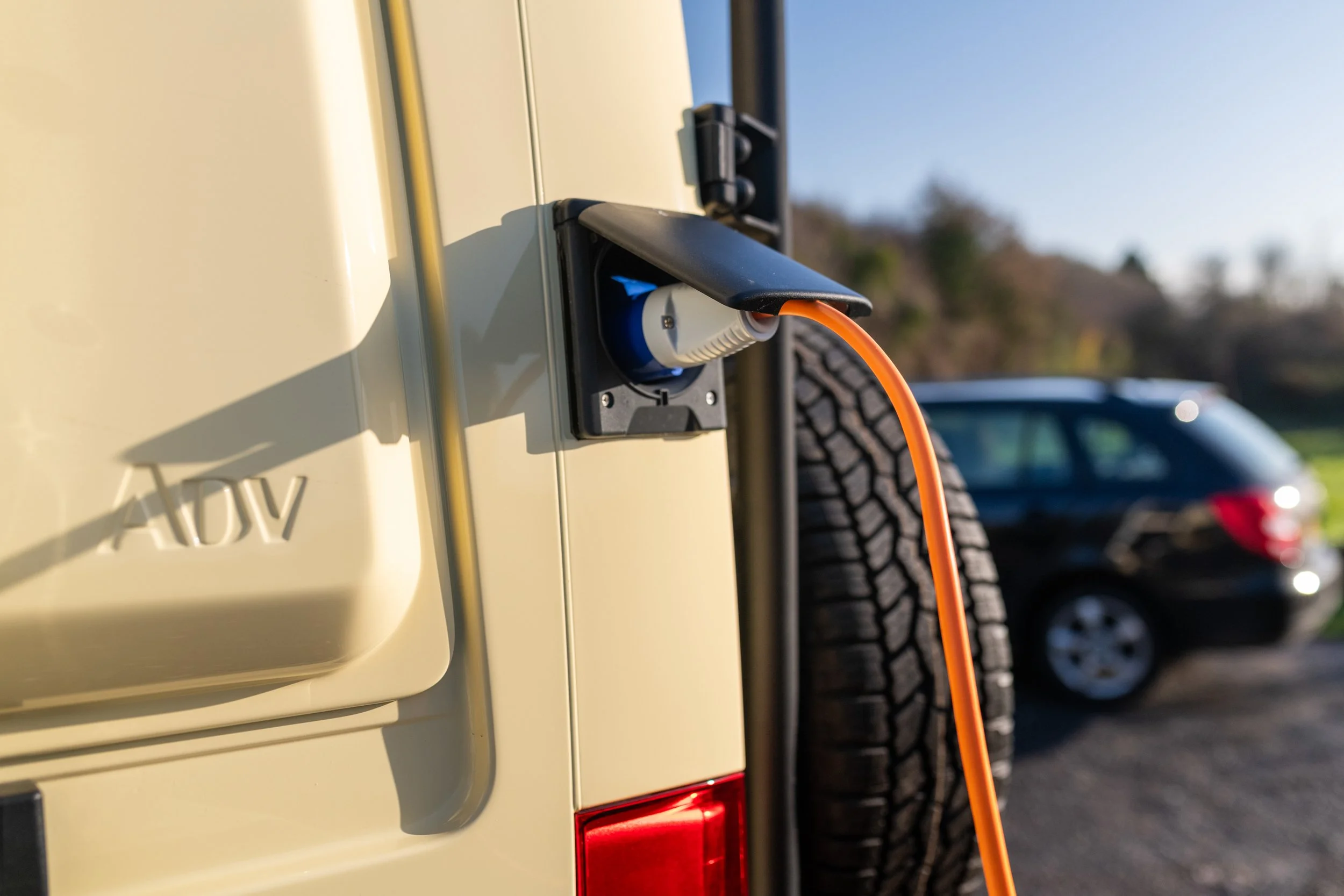 Orange hook-up cable plugged into the Fern campervan’s rear shore power inlet, allowing battery charging and direct mains power when parked.