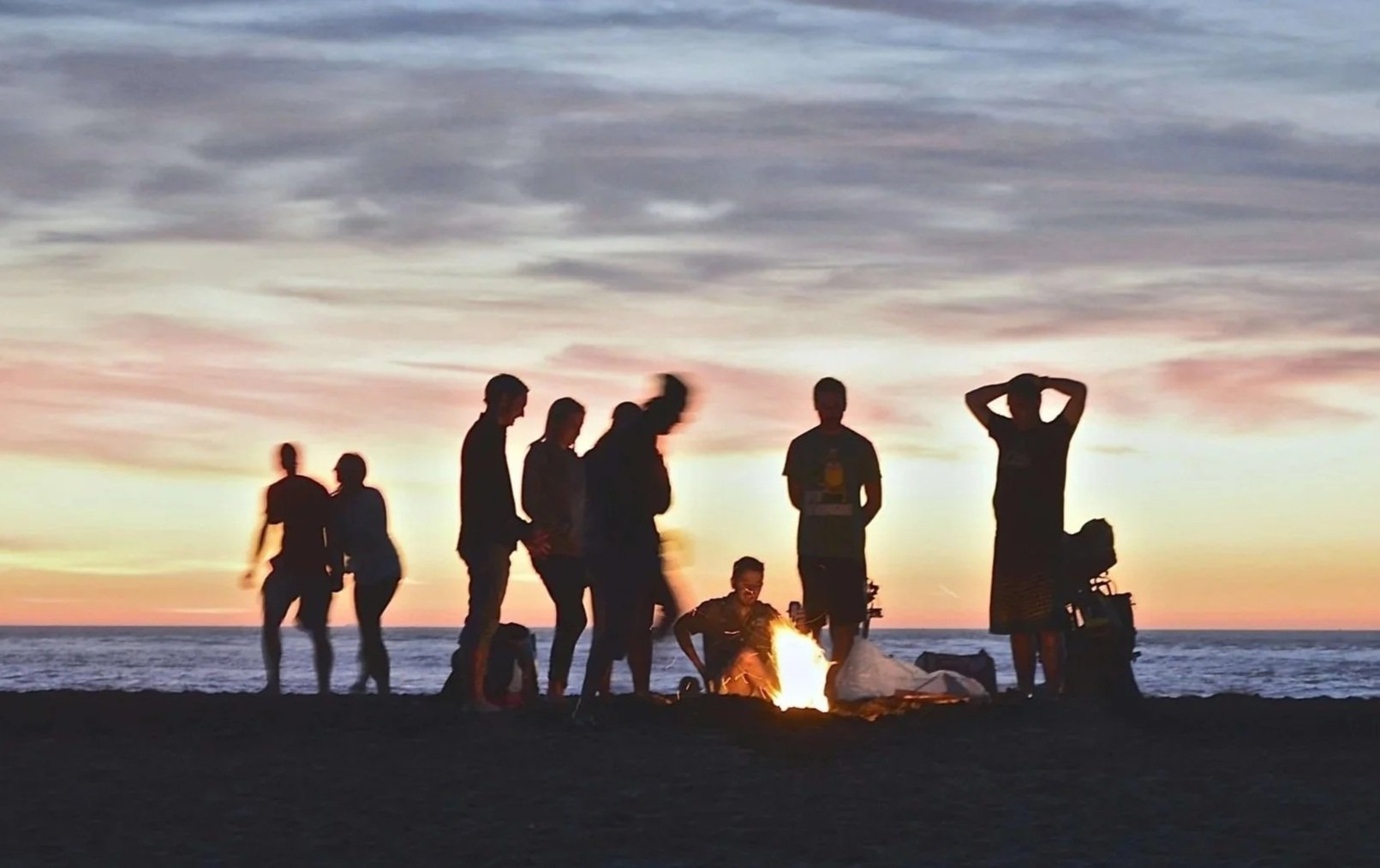 Group of people gathered by a bonfire on the beach at sunset