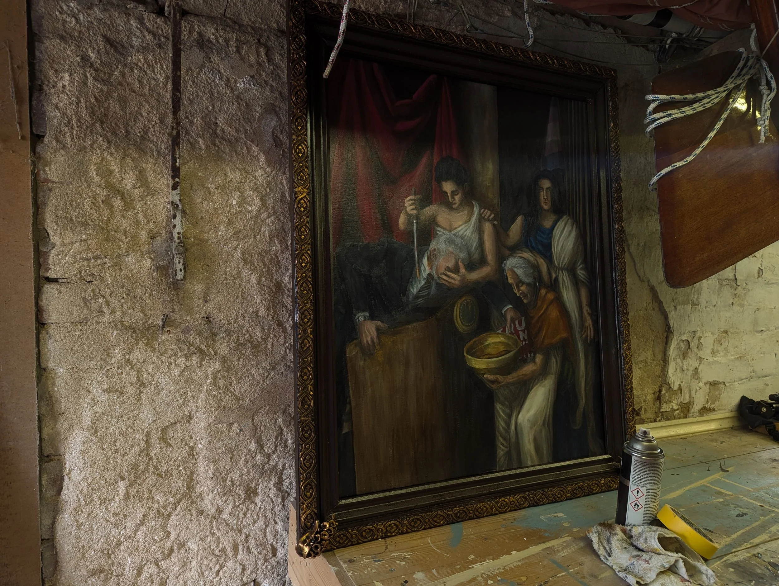 The completed painting of 'The Coup d'etat of Midas' in its frame. Propped up against a whitewashed brick wall on a wooden worktop.