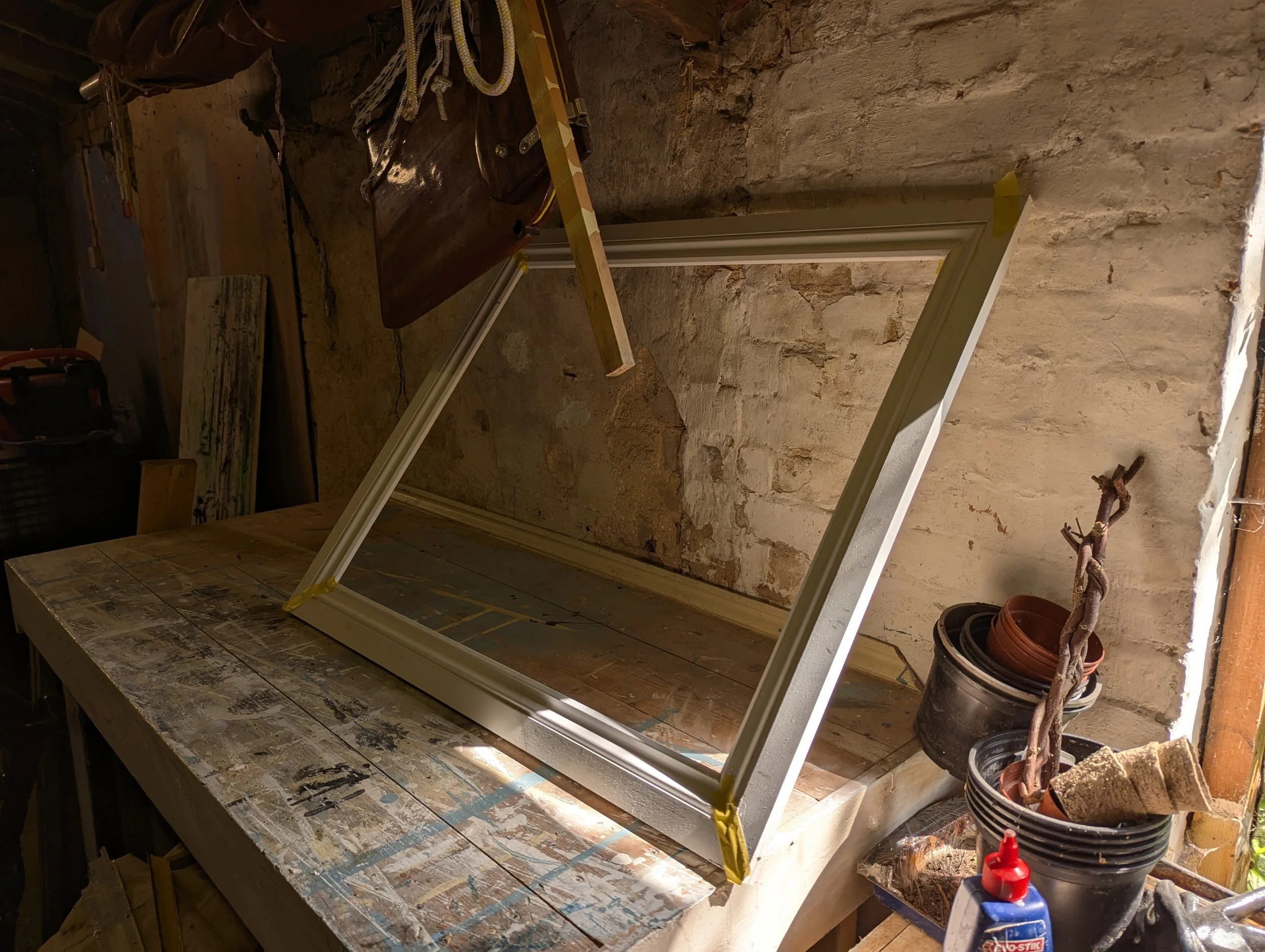 Partially made frame for 'The Coup d'etat of Midas'. Propped up against a whitewashed brick wall with taped up edges.