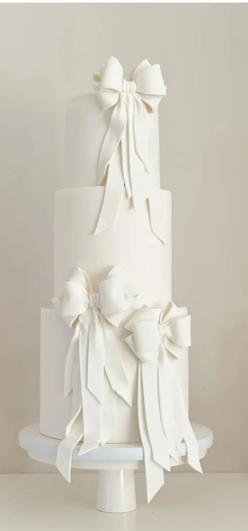 Three-tiered white wedding cake decorated with white, pink, and purple flowers and green leaves, placed on a silver cake board on a white tablecloth.