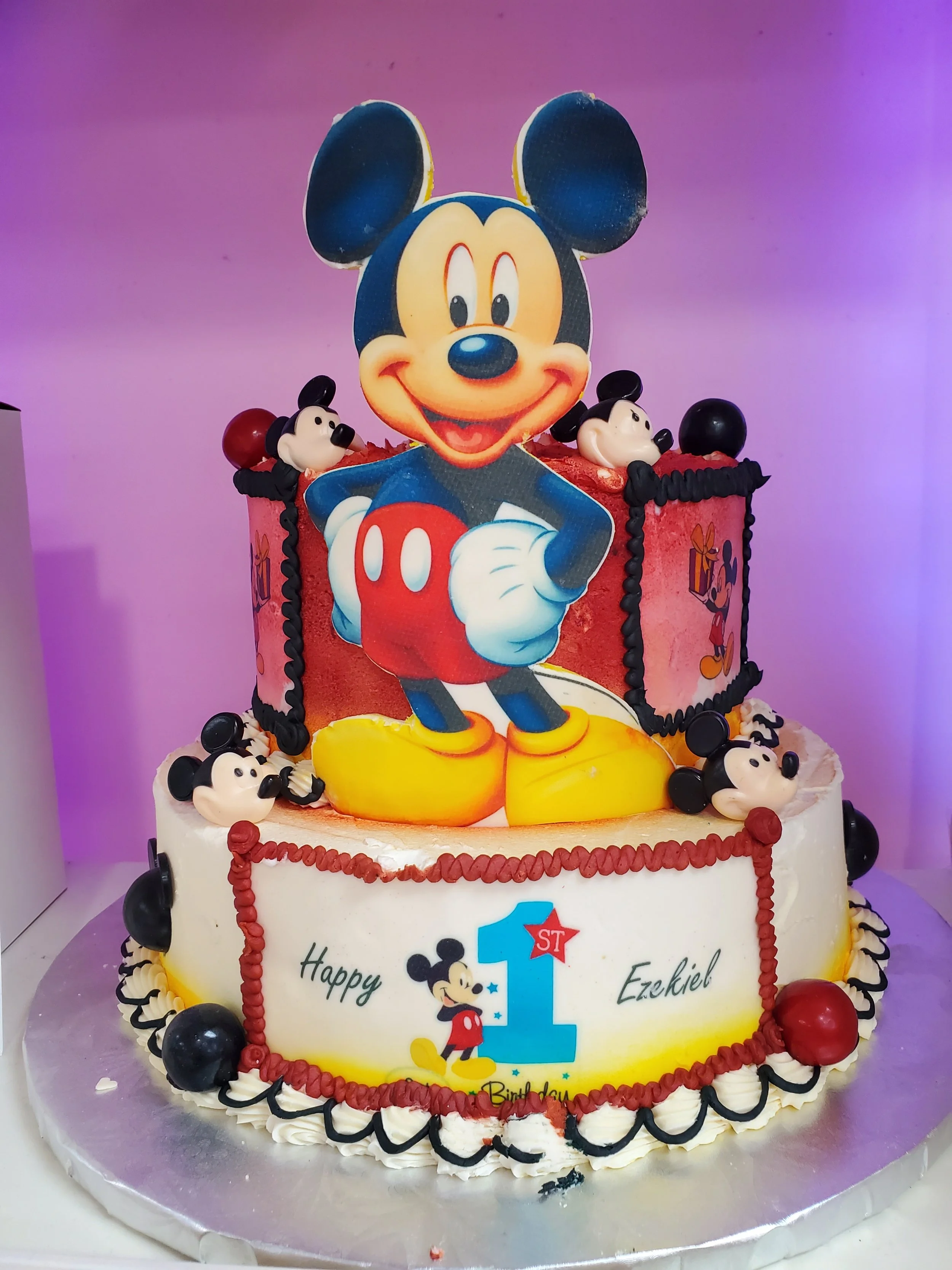 The Mick Mouse themed birthday cake for a first birthday, featuring a large Mick Mouse figure, and colorful decorations with a pink and white base.