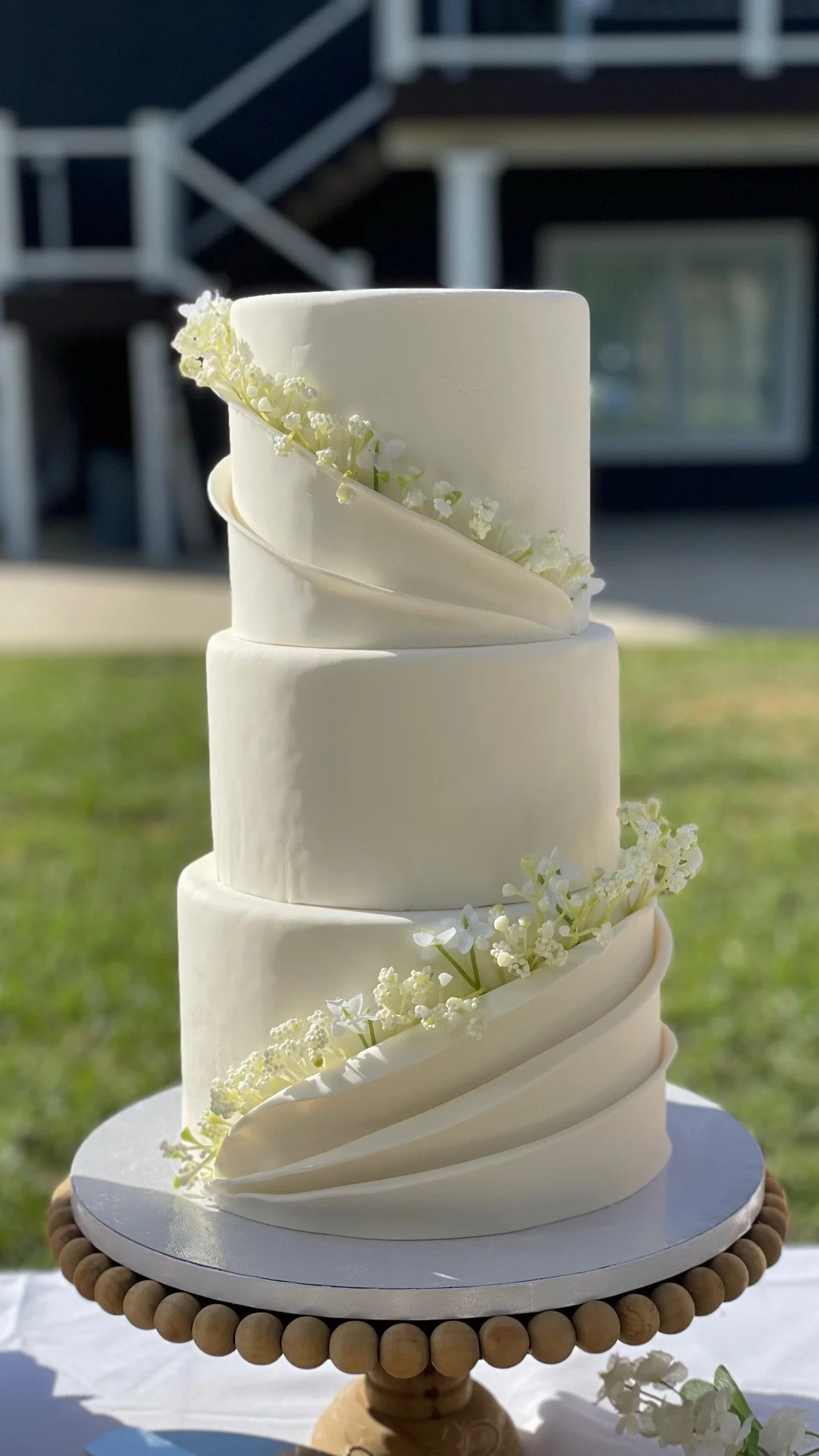 Four-tier white wedding cake decorated with white flowers and white fondant drapes, simple but belegant.