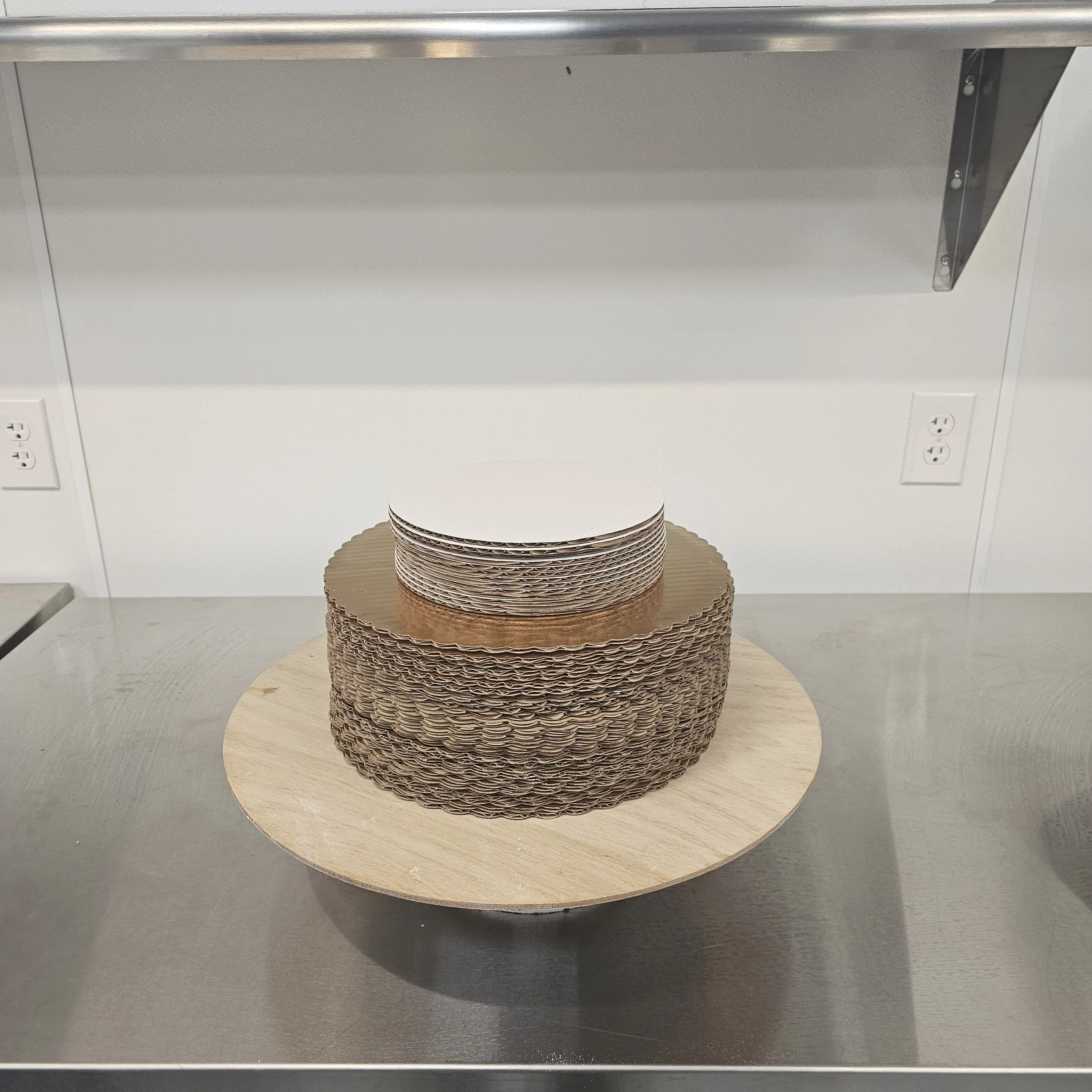 A two-tier birthday cake with gold and black decorations, featuring a bottle of Rémy Martin cognac with a red and black VIP label on top, and a large gold number 26 in front. The cake has black accents resembling worm-like shapes and black spheres around the edges, with a message written in black icing on the white base.