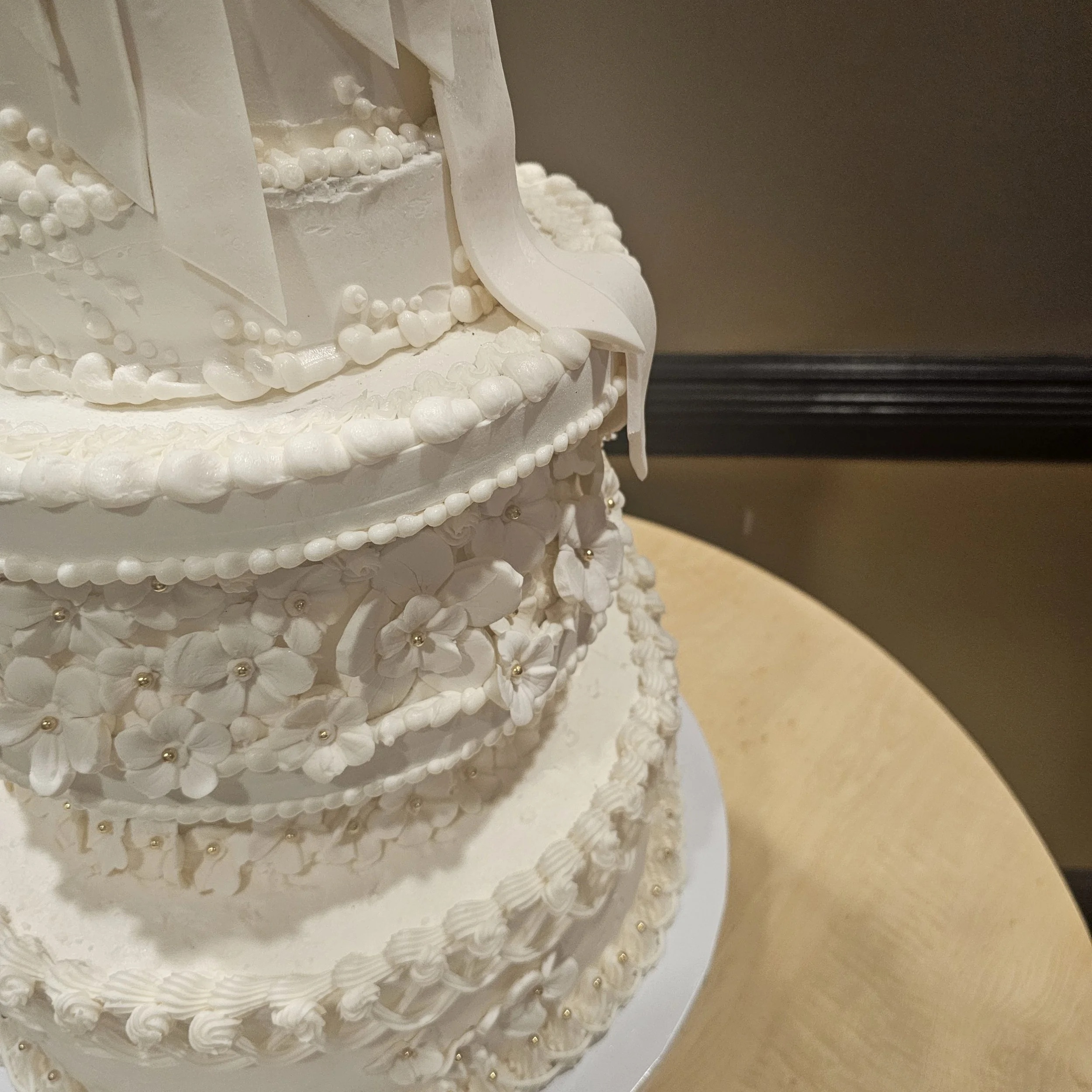 Pink and white birthday cake with a large gold '50' topper, decorated with pink icing drips, silver beads, and gold accents, with a heart-shaped plaque that says "Lachelle."