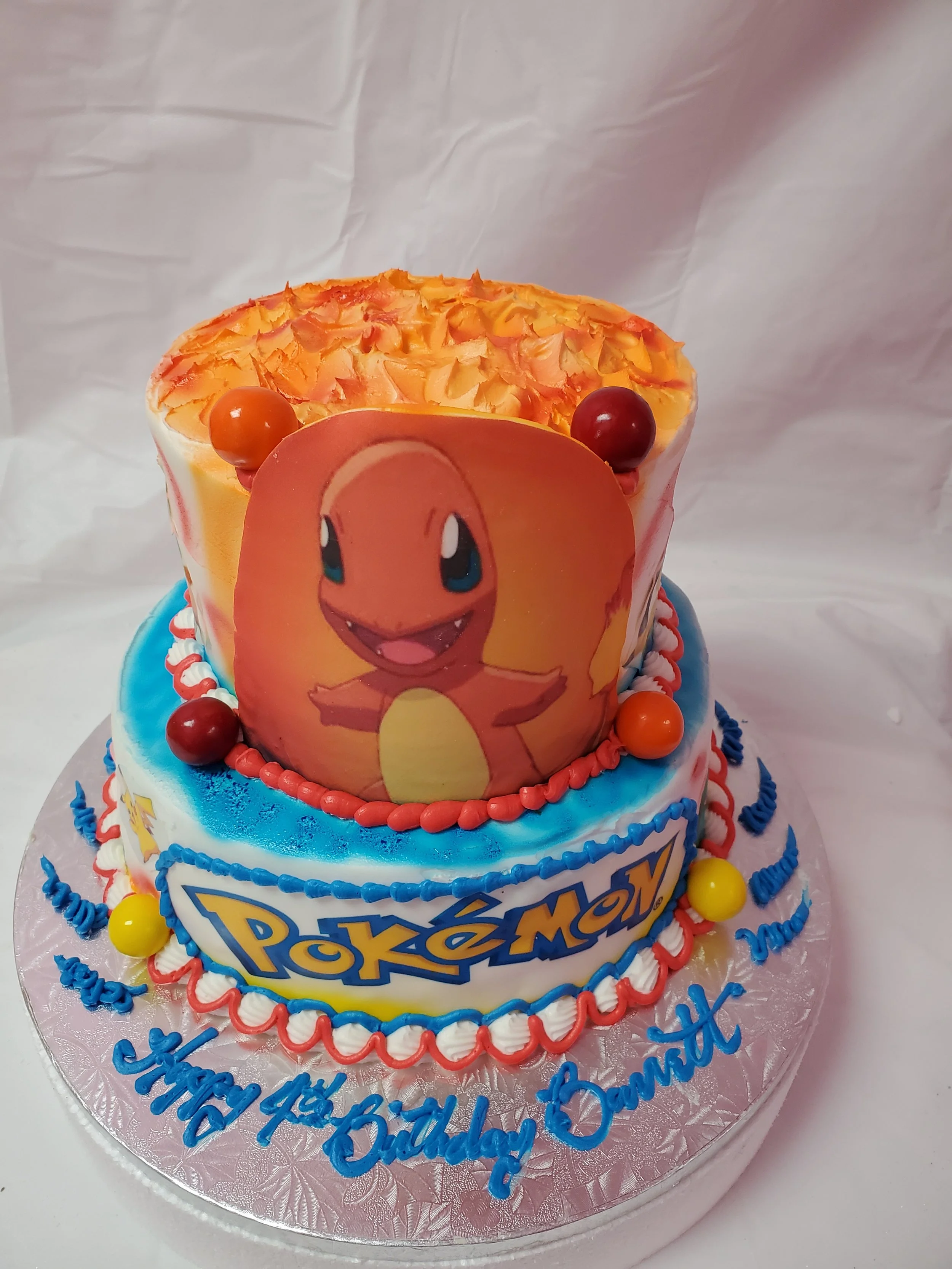 A Pokémon-themed birthday cake featuring a large image of Charmander, with orange, red, yellow, and blue decorations, and the words "Happy Birthday Darren" written in blue icing.