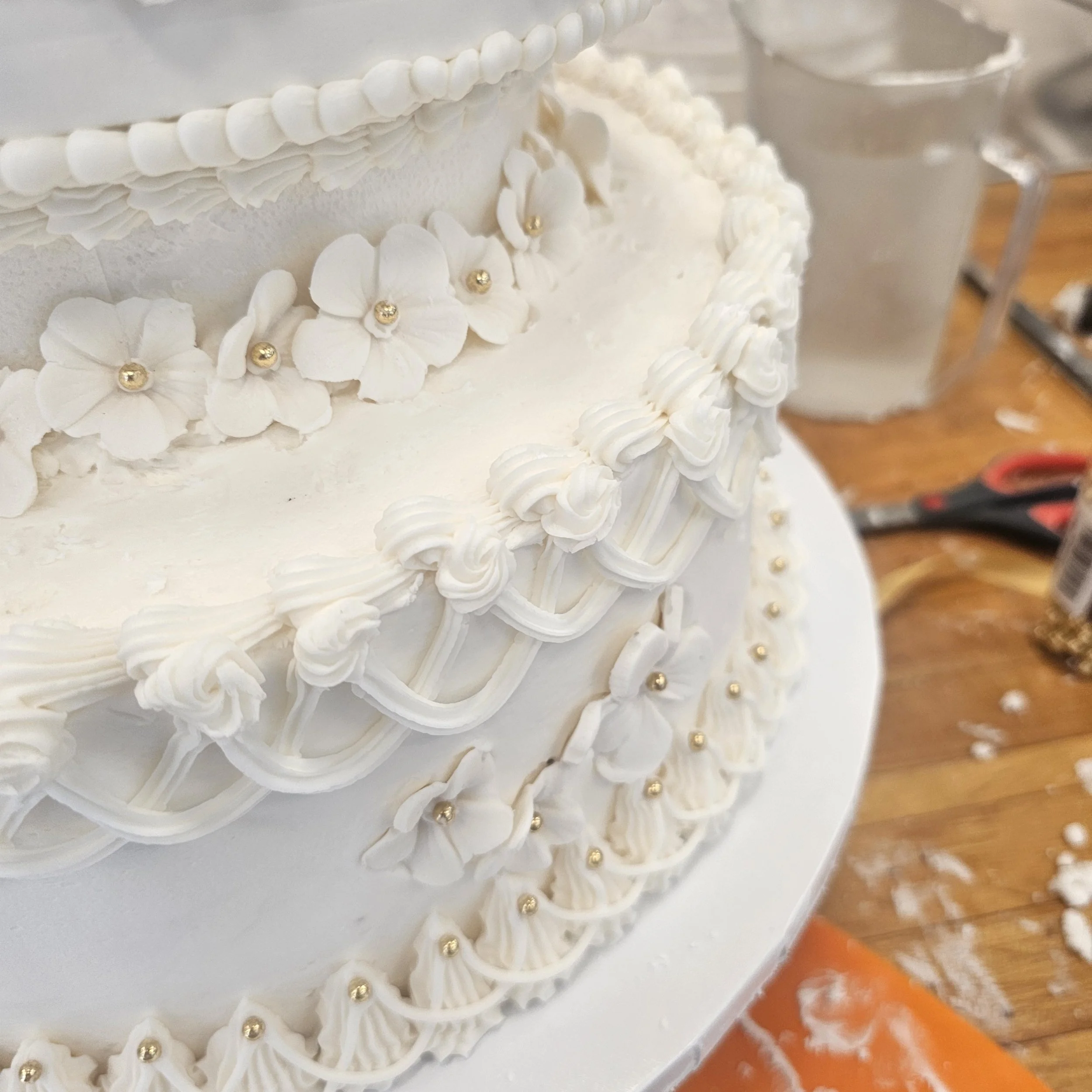 A two-tiered birthday cake with a zebra and jungle animal theme, featuring a printed topper of animals like a giraffe, zebra, lion, elephant, and hippopotamus with tropical leaves, decorated with black zebra print frosting and green, black, and yellow frosting accents.