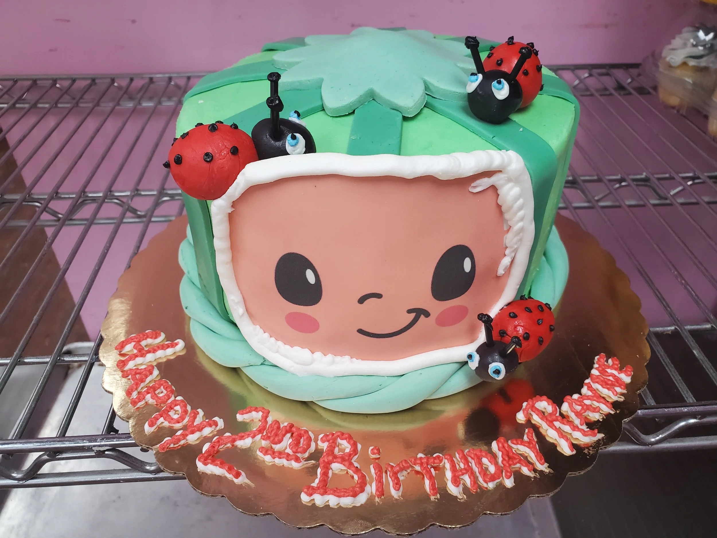 Colorful birthday cake with a cartoon face decoration, ladybug and caterpillar toppers, and a message reading 'Happy Birthday Maren' in red icing