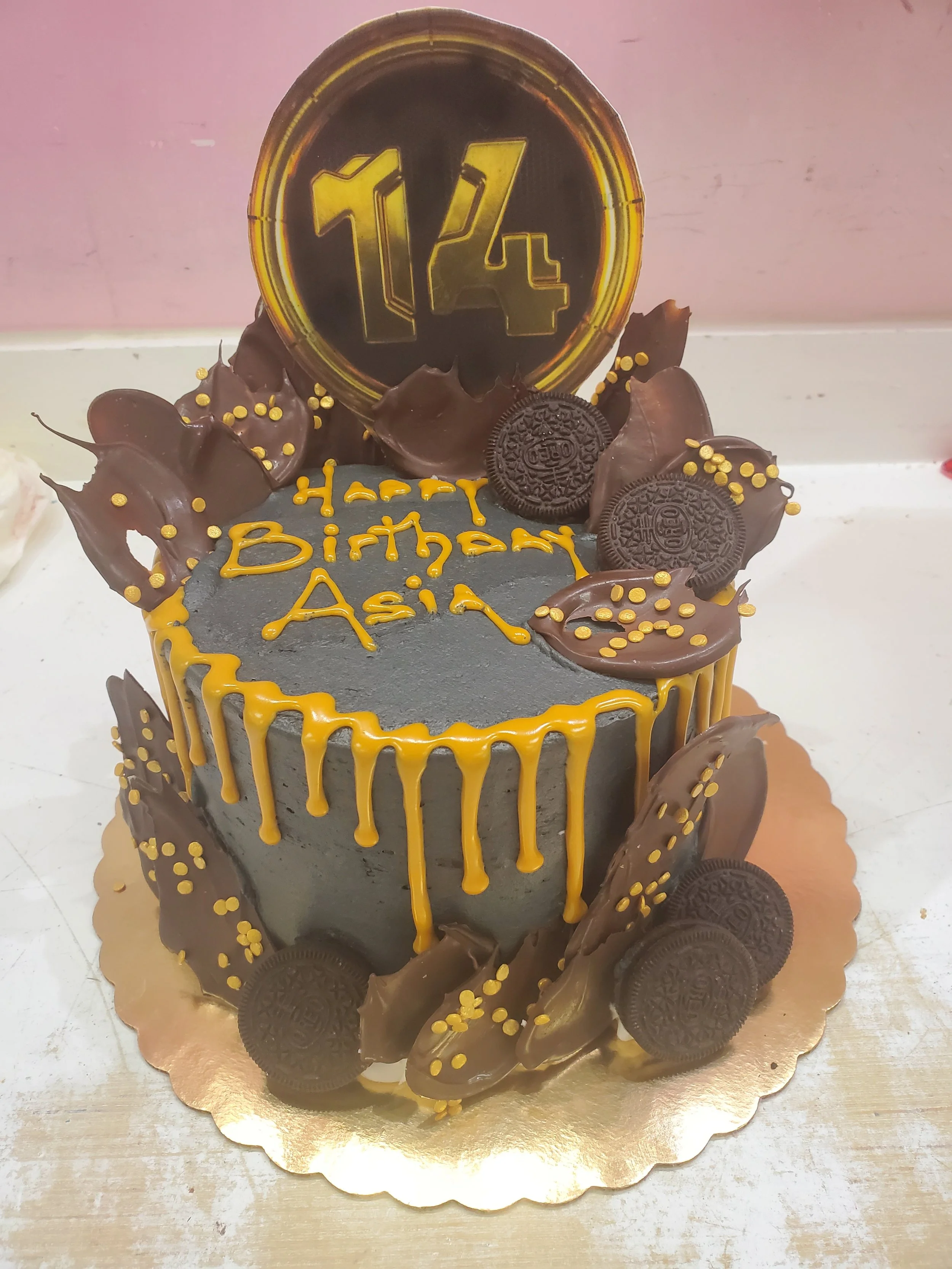Black and gold birthday cake with chocolate Oreos and yellow drizzle, celebrating Asia's 14th birthday.