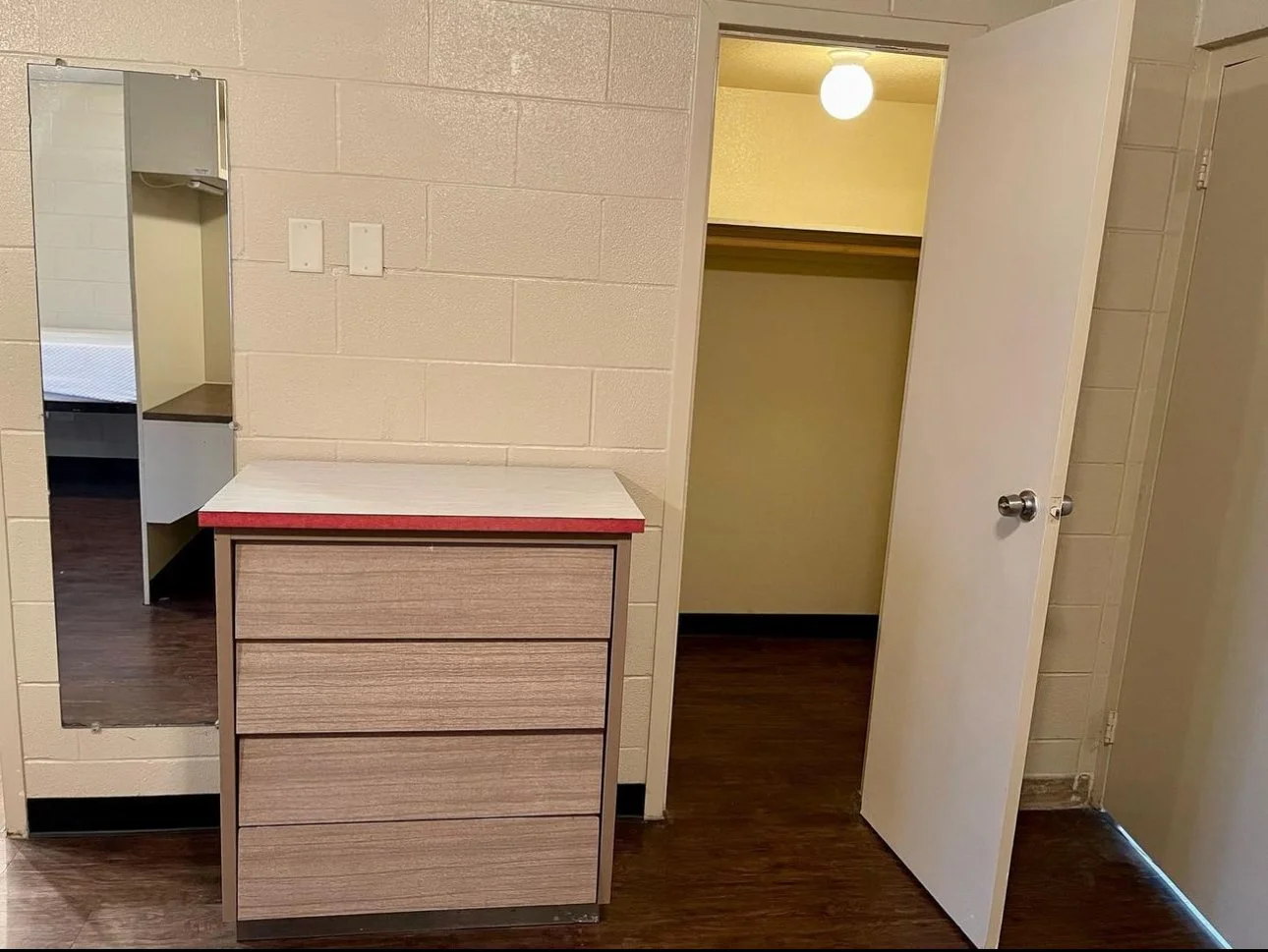 This furnished dorm room offers a simple, functional living space designed for comfort and study. Each resident has a twin bed with under-bed storage, a personal desk with shelving, and built-in closet space. The open layout provides ample room to mo