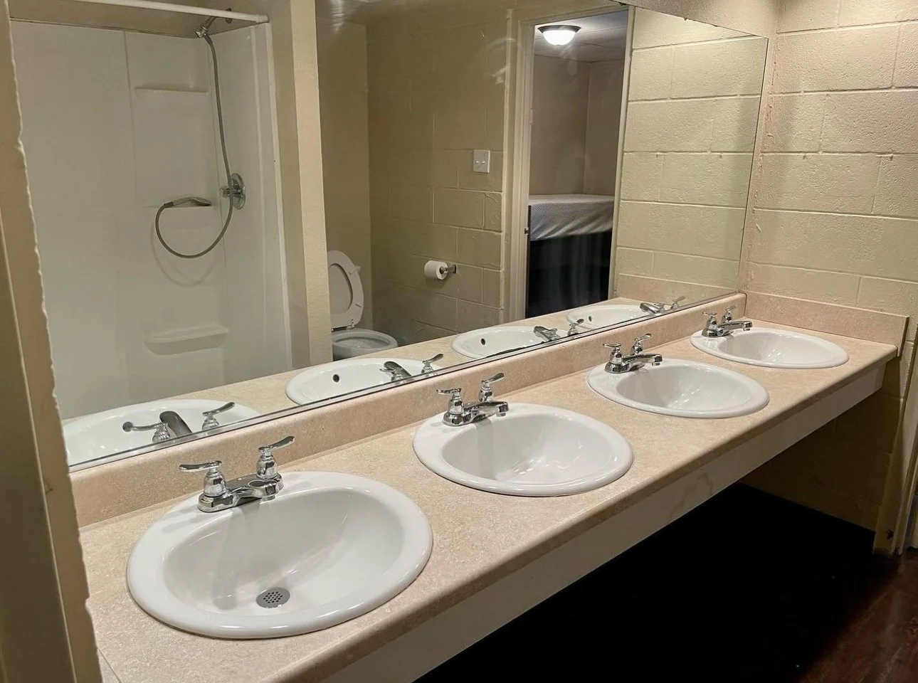The shared bathroom features multiple sinks with a large mirror, providing convenient space for daily routines. It includes private shower and toilet area, designed for ease of use and efficiency while serving residents comfortably and practically.