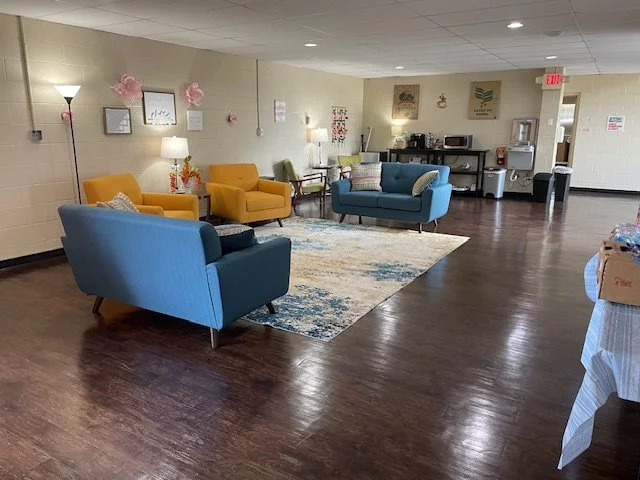 Community lounge with colorful armchairs, wall decorations, and a coffee station in the background.