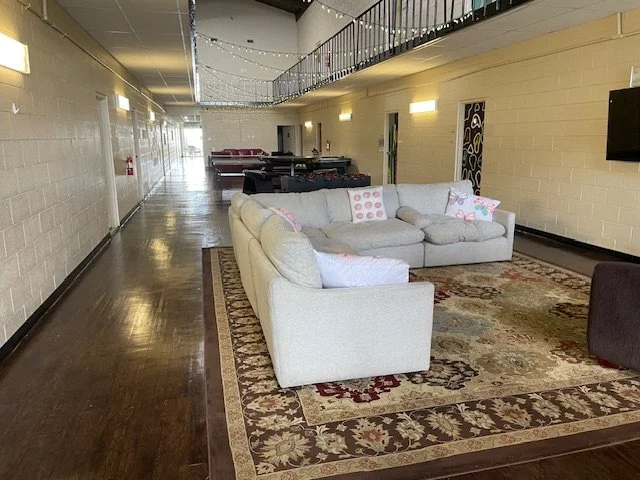 A lounge area with a white sectional sofa on a patterned rug in a spacious hallway.