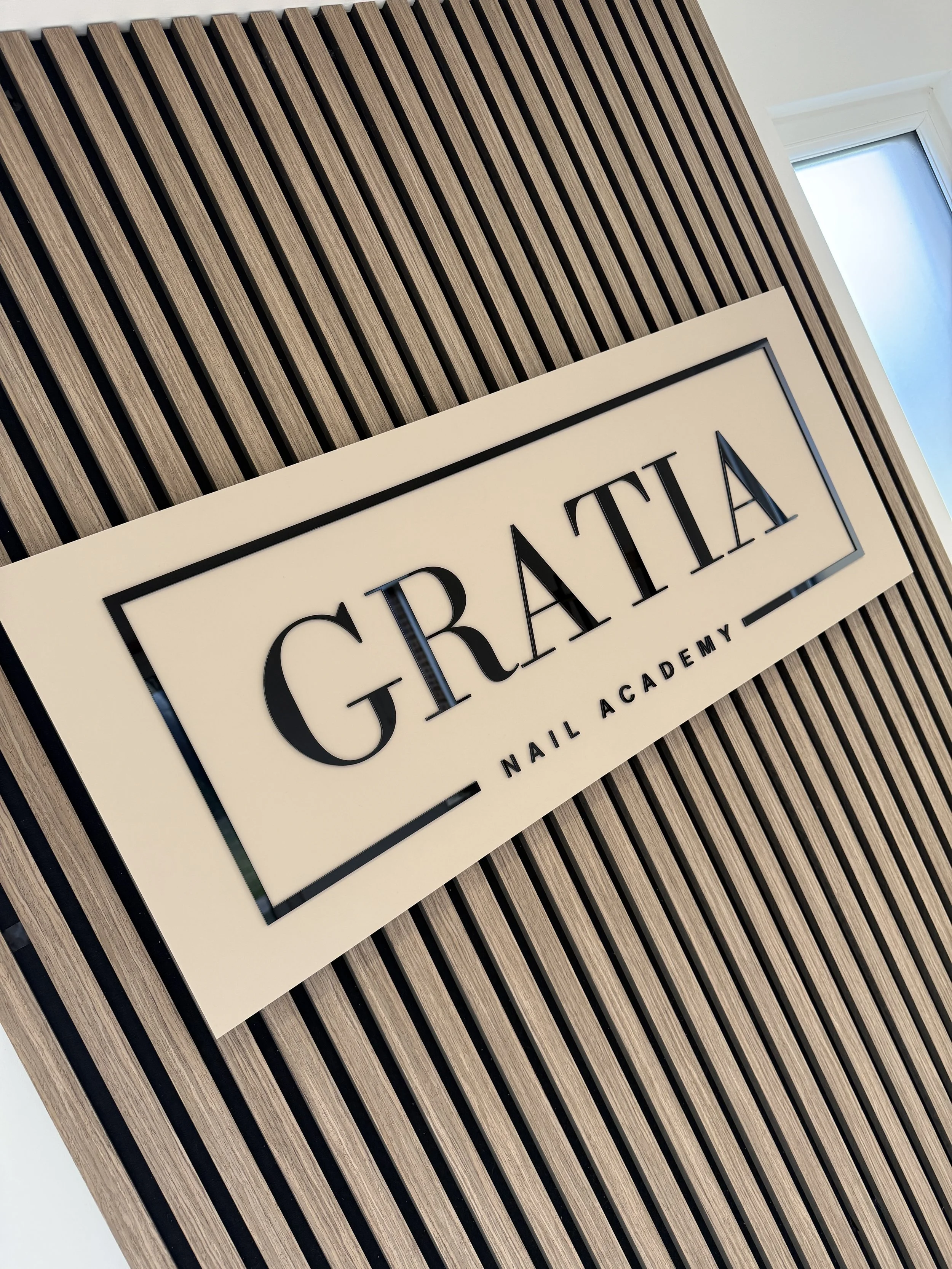 Close-up of a sign that reads 'GRAIL' on a wooden slatted wall with a window nearby.